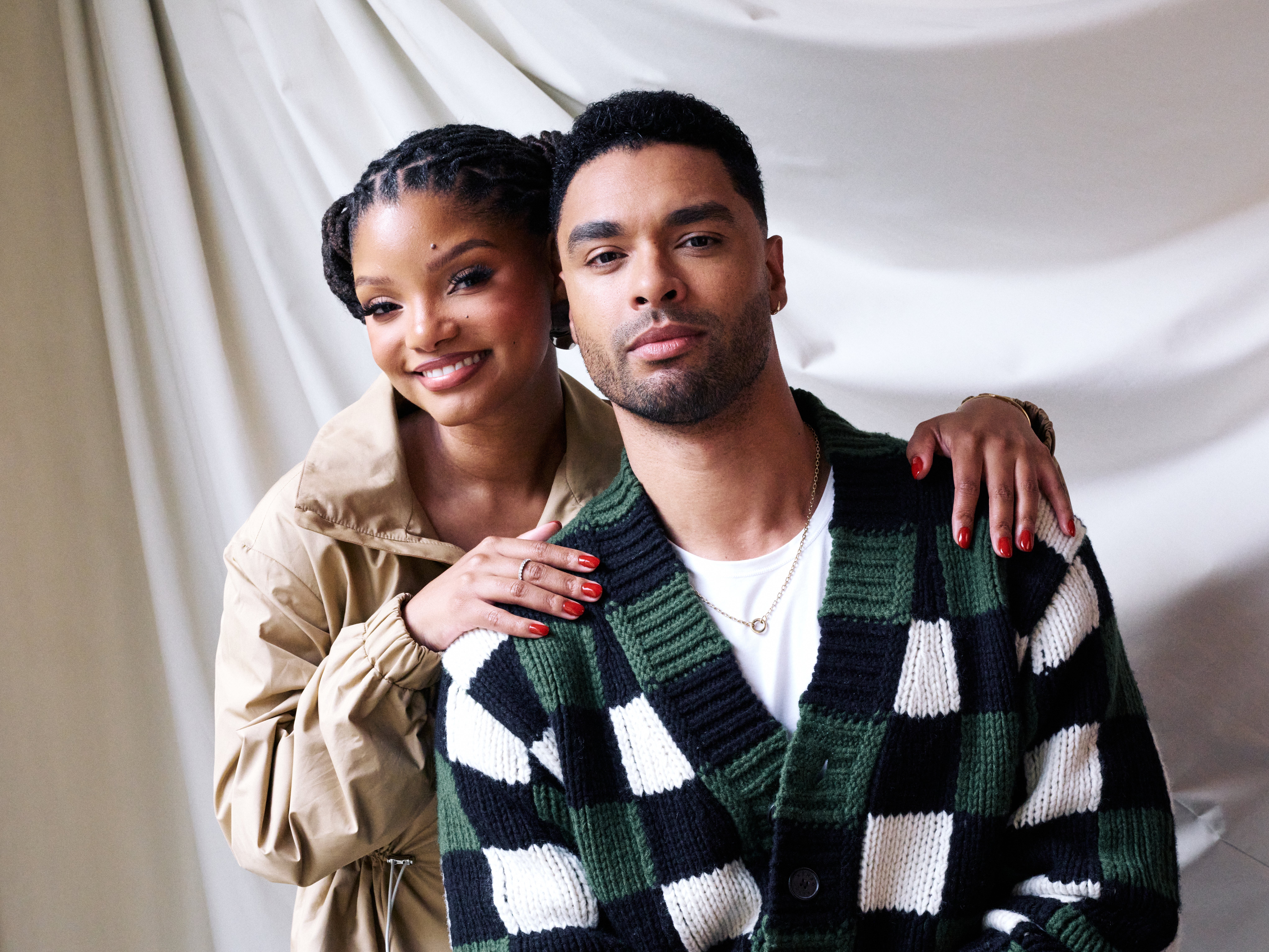 To personer poserer sammen, den ene med flettet frisyre, iført en beige jakke, og den andre i en rutete cardigan. Begge smiler varmt