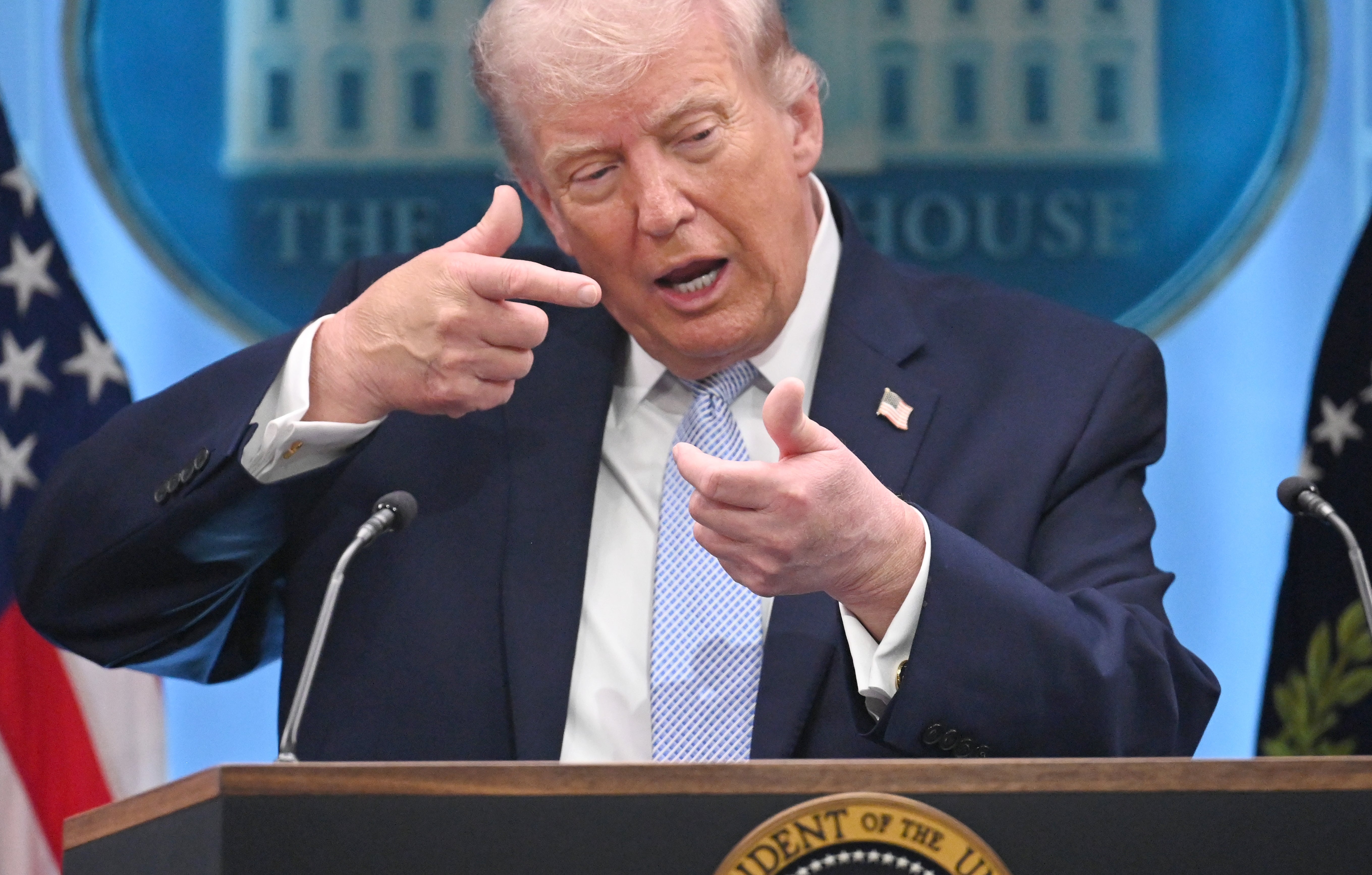 Mann gestikulerer under en pressekonferanse på et podium med presidentens segl. Bakgrunnen viser amerikanske flagg og et emblem fra Det hvite hus