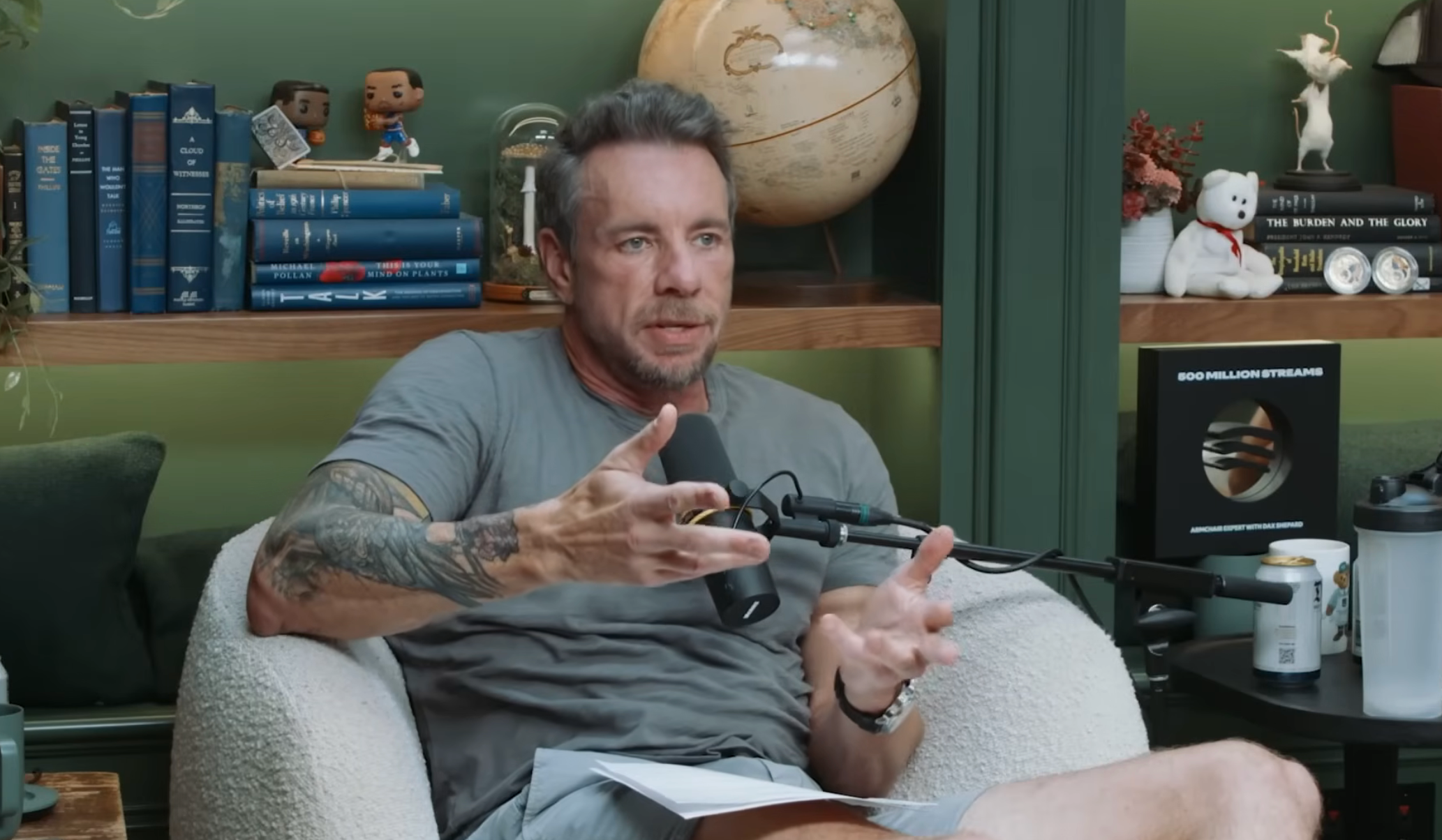 Man sitting successful a cozy room, speaking into a podcast microphone, gesturing with his hands, surrounded by books and decorative items