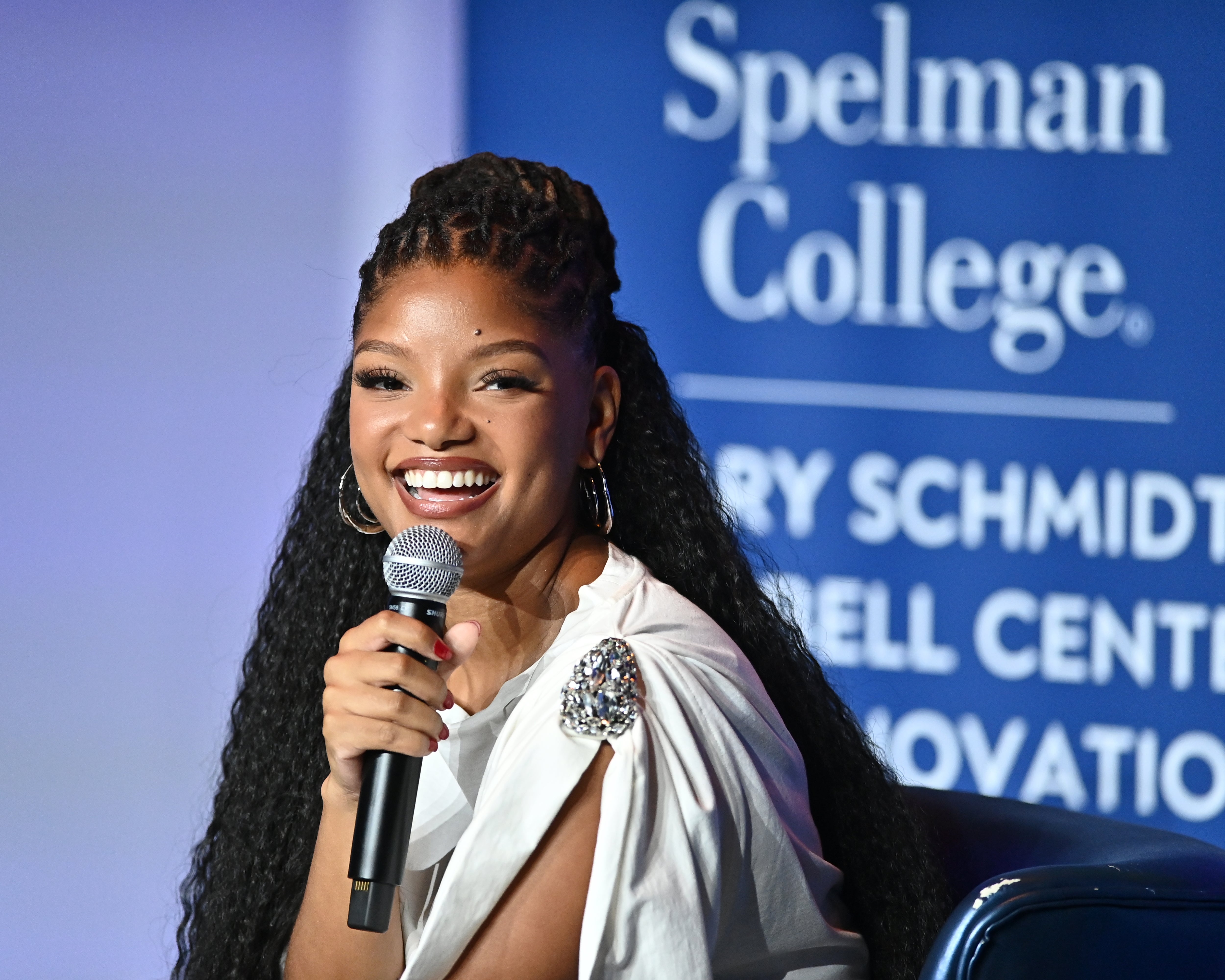 Person som smiler, holder en mikrofon, iført en hvit topp med en juveldetaljer på skulderen på et Spelman College-arrangement