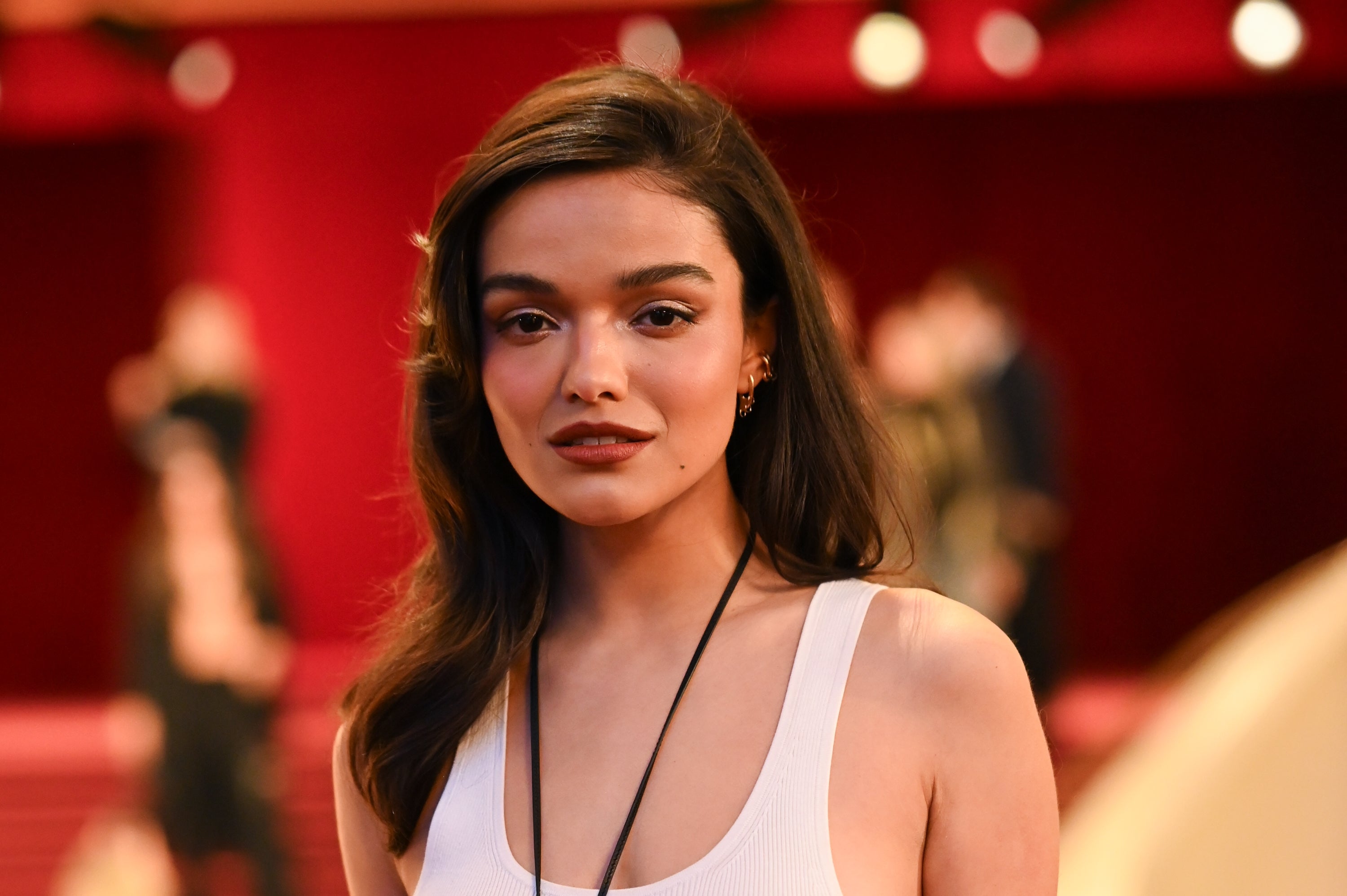 Person på en rød løper i en ermeløs topp, med langt hår stylet naturlig, ser selvsikkert på kameraet