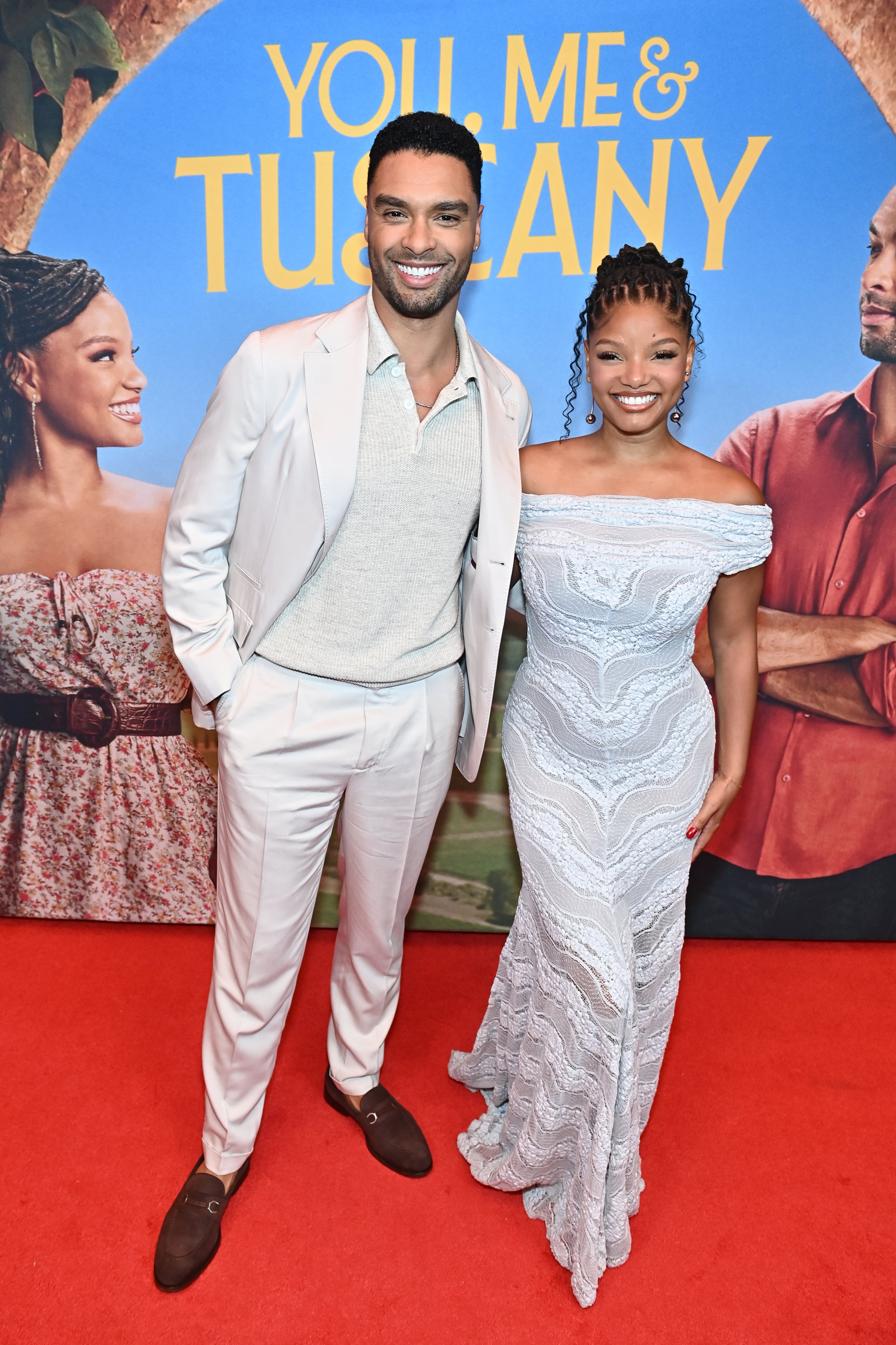 To personer på en rød løper; den ene i en lys dress, den andre i en lacy off-shoulder-kjole, poserer foran en 