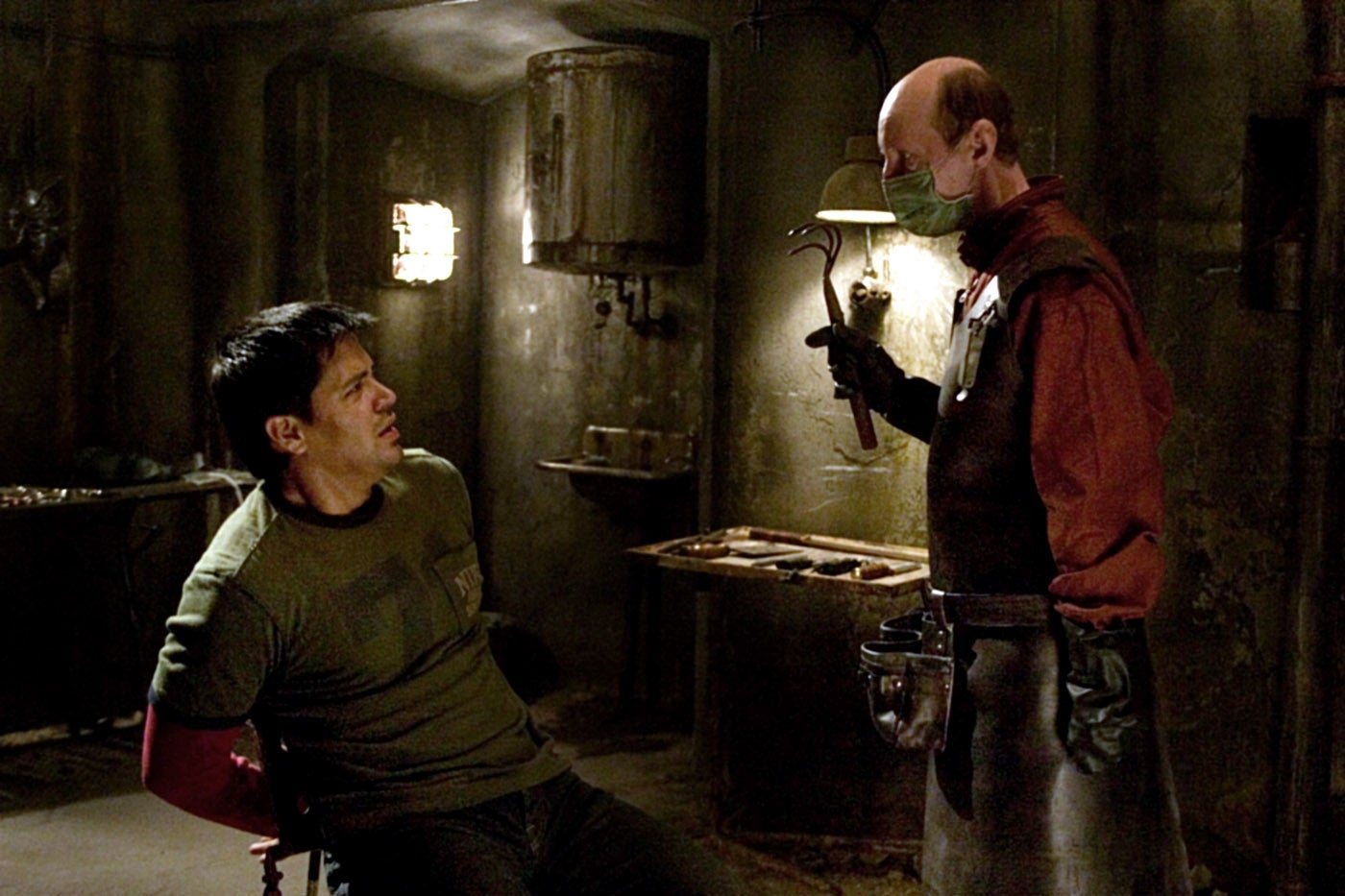 A idiosyncratic tied to a seat looks astatine different wearing a surgical disguise and apron, holding a instrumentality successful a dimly lit, ominous room