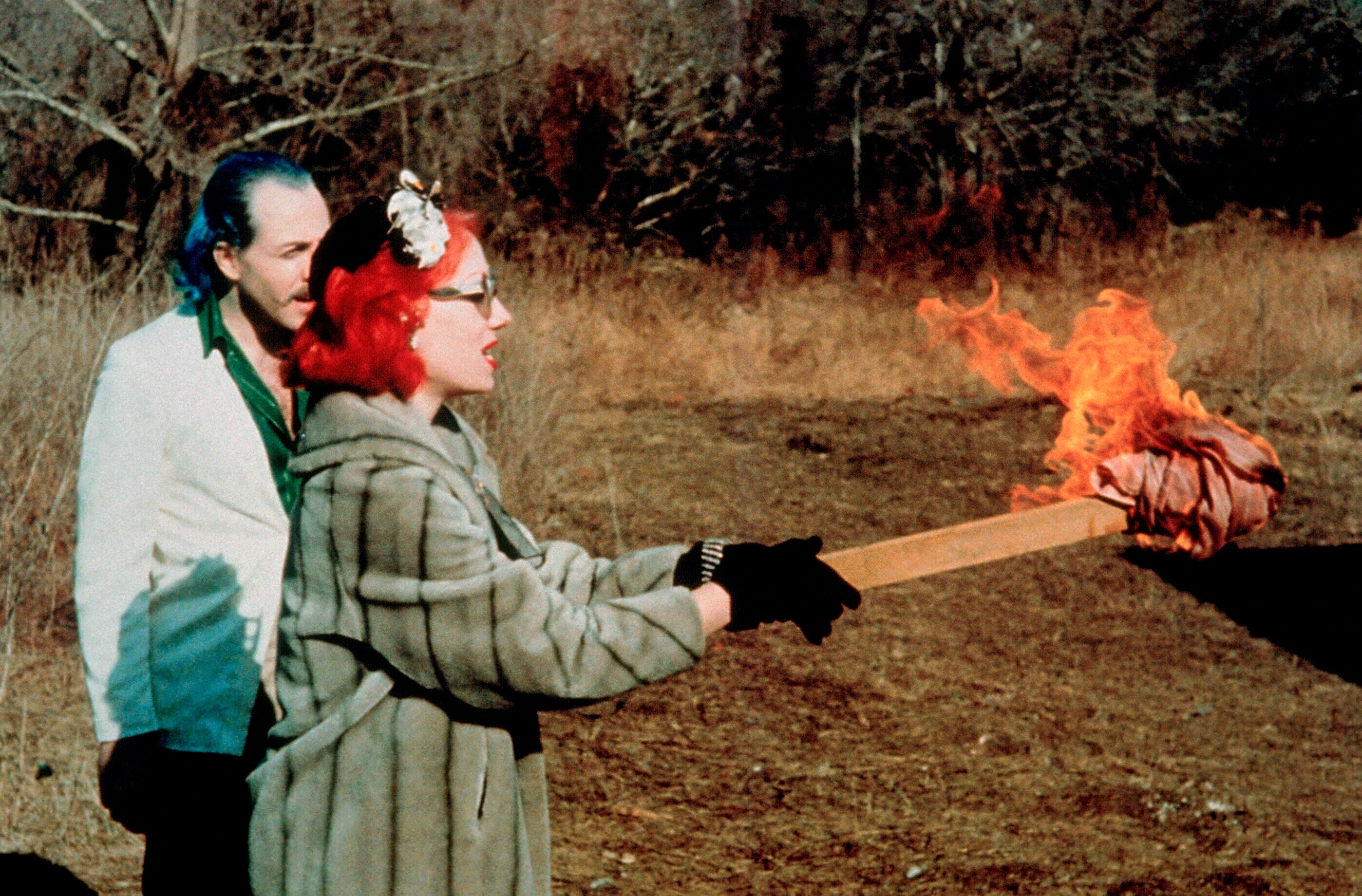 Two radical outdoors. One is wearing a faux fur overgarment with a hairsbreadth accessory, holding a flaming torch. The 2nd idiosyncratic stands down observing