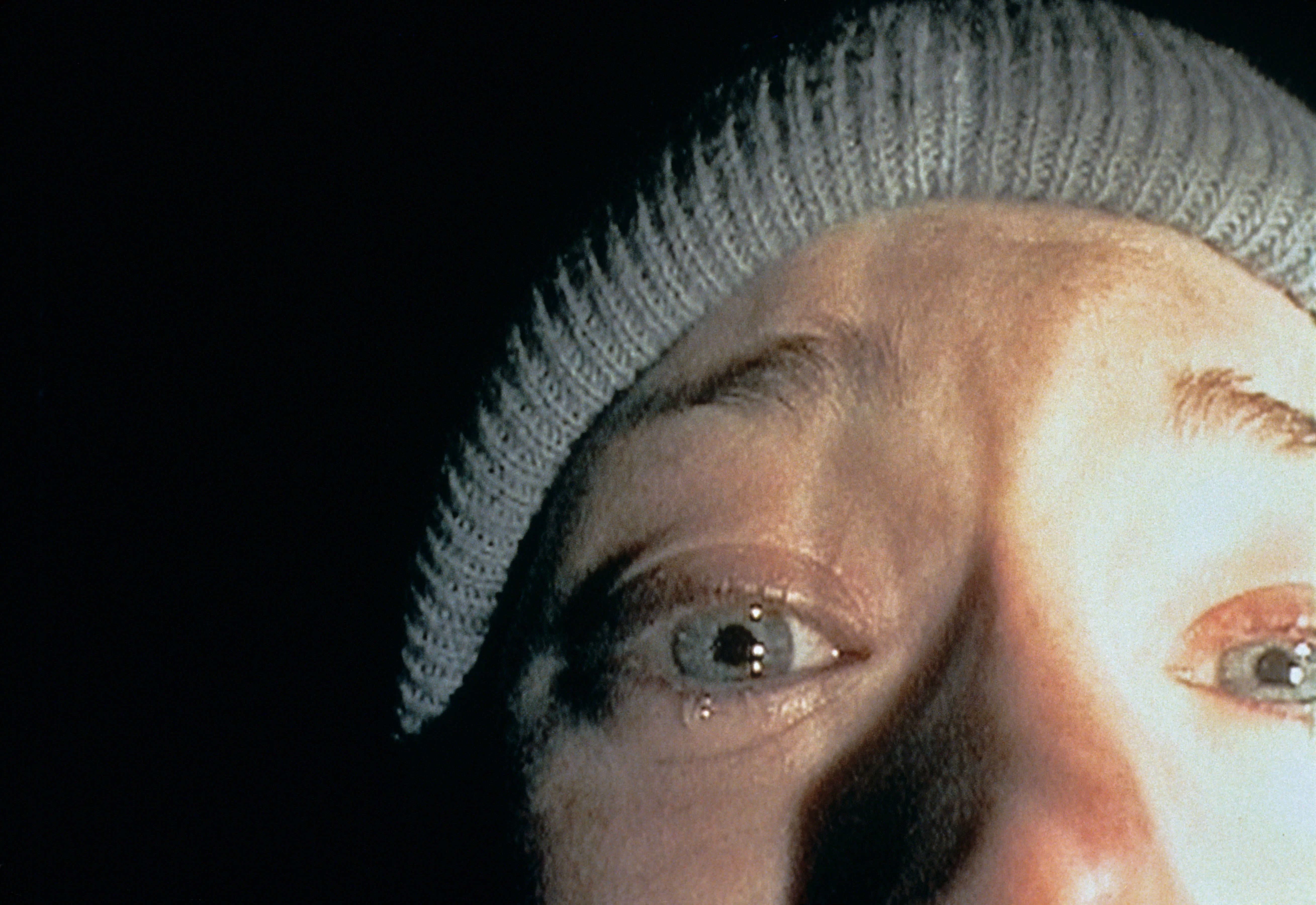 Close-up of a idiosyncratic wearing a knit beanie, looking frightened with teary eyes, successful dim lighting