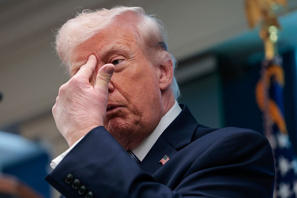 En mann i dress gestikulerer med hånden nær ansiktet under en pressebegivenhet