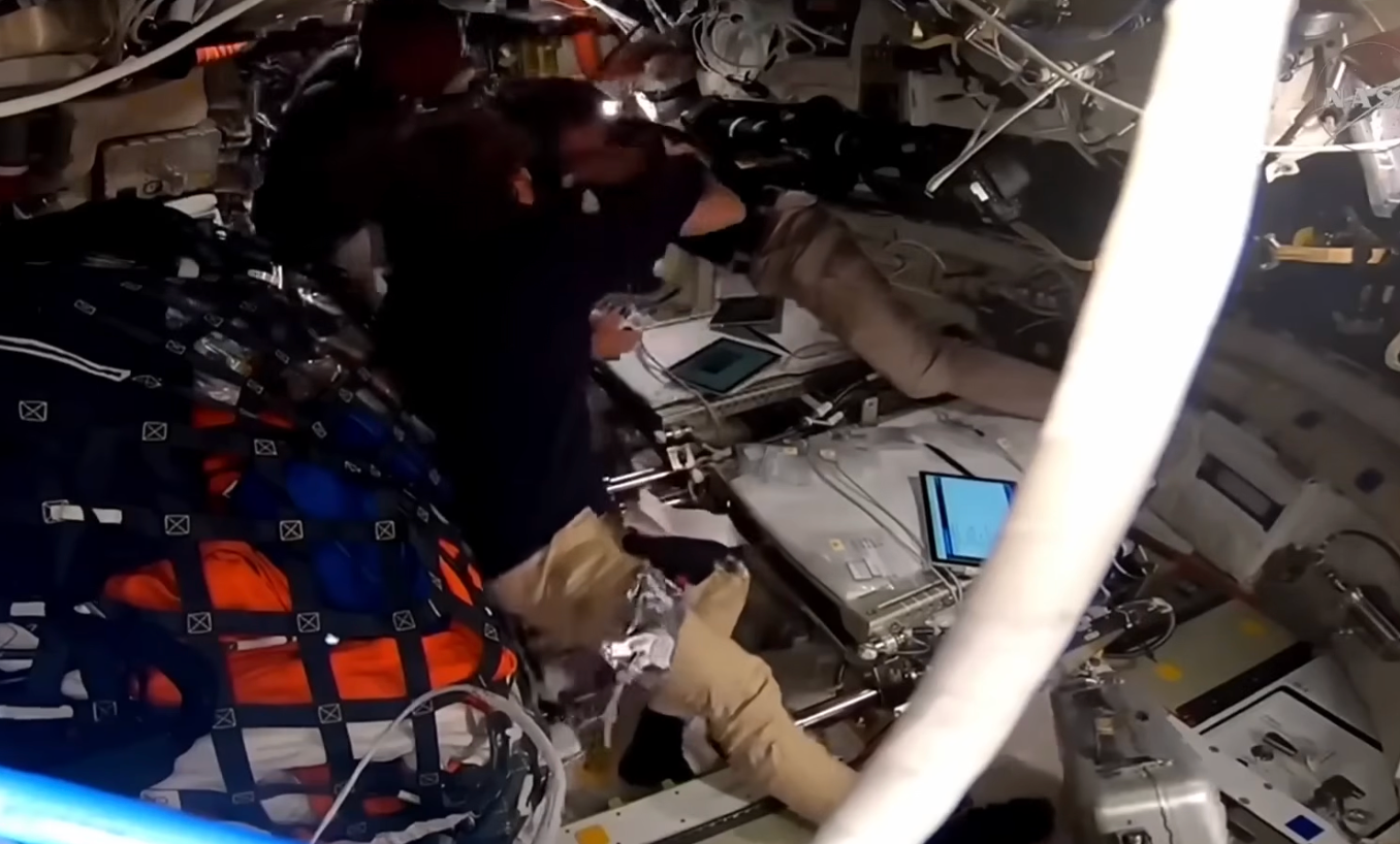 Astronauter inne i et romfartøy, omgitt av utstyr og skjermer, ser ut til å være engasjerte i oppgaver under et oppdrag