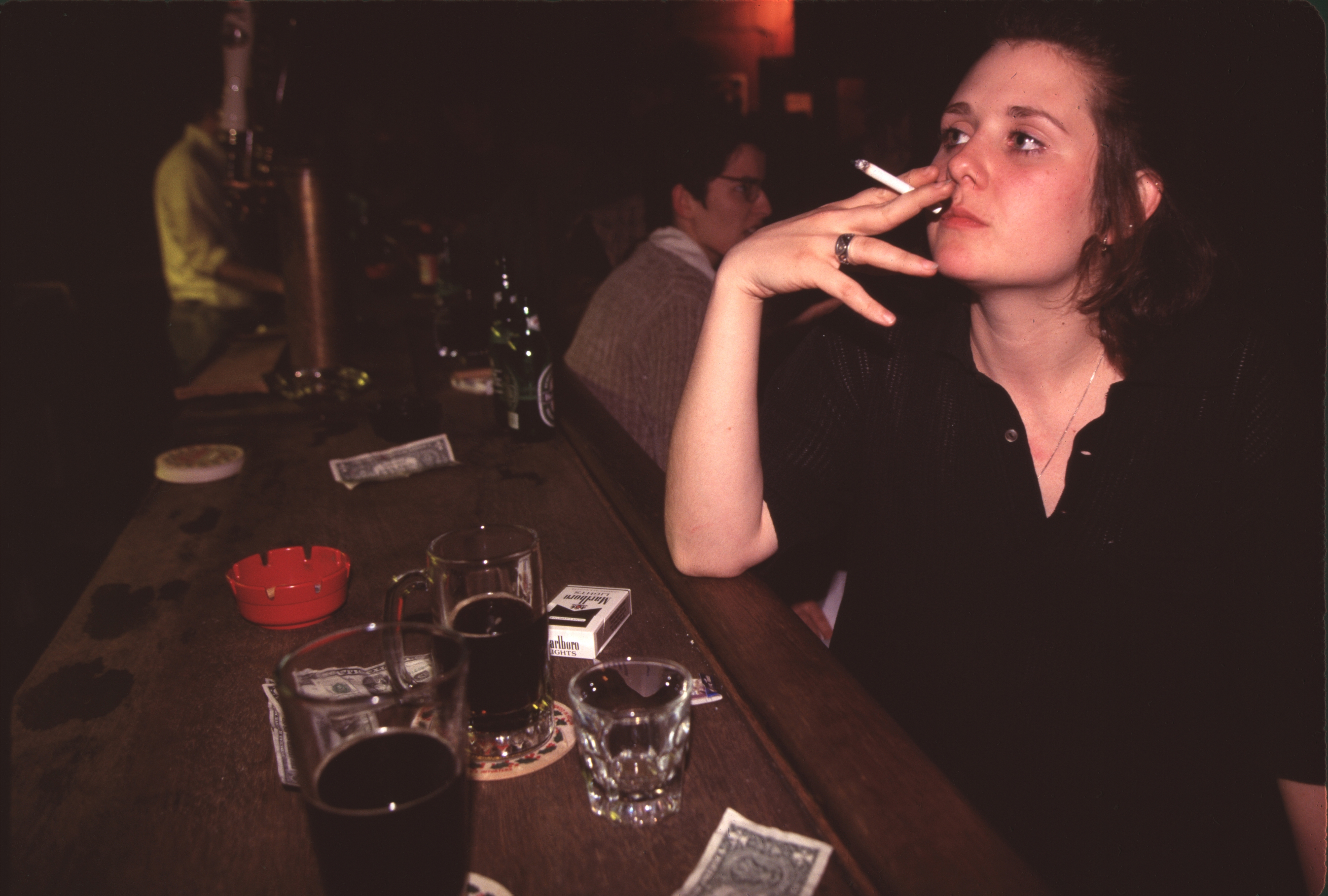 Person sitting astatine a barroom antagonistic with drinks and money, holding a cigarette, appearing contemplative successful a casual setting