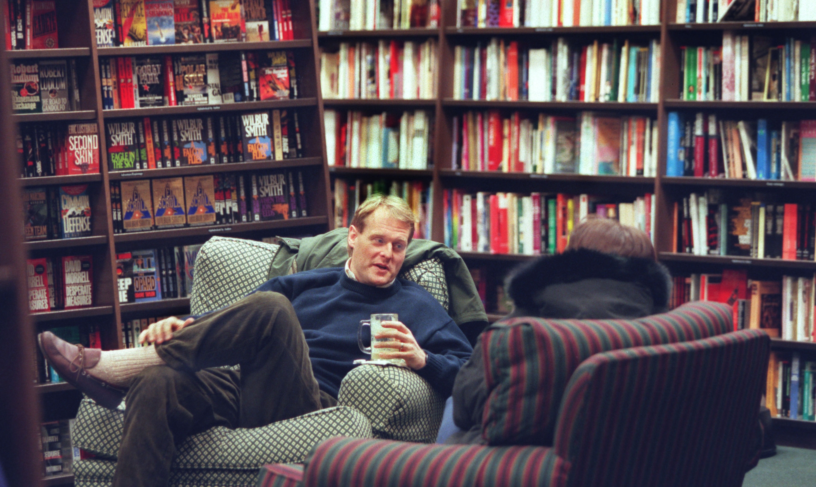 Two radical are sitting successful a cozy bookstore, engaged successful conversation, surrounded by shelves filled with books