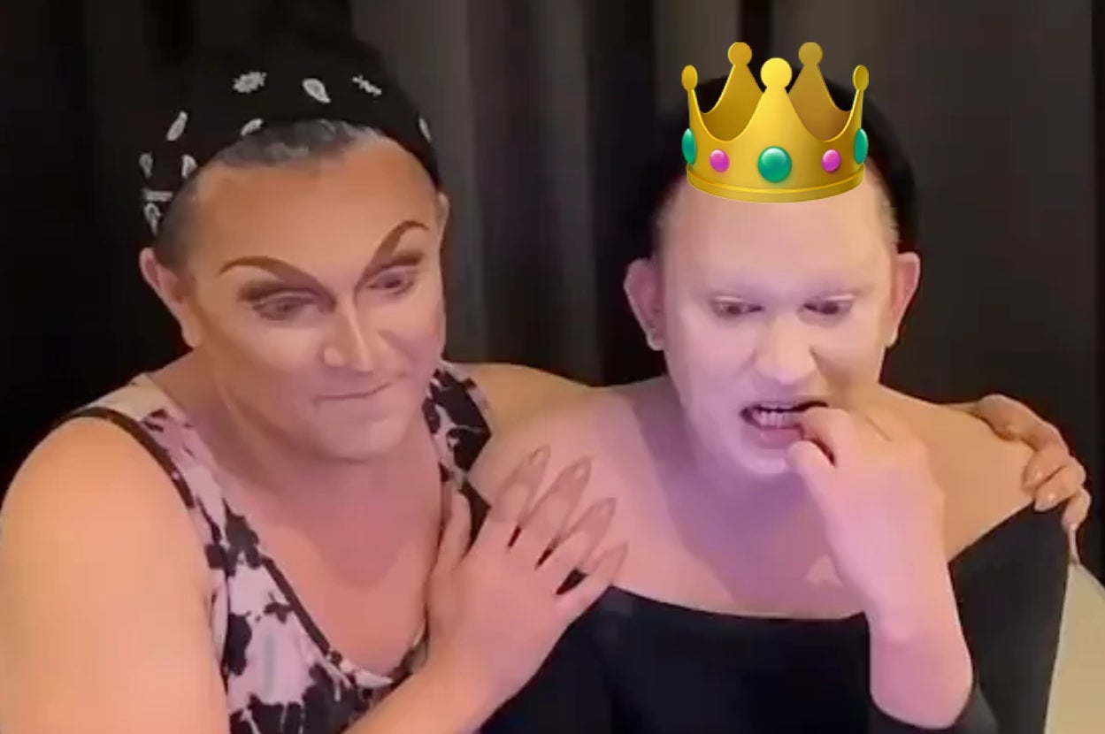 Two individuals in drag makeup, one wearing a floral dress and bandana, the other with a digital crown, sharing a moment backstage