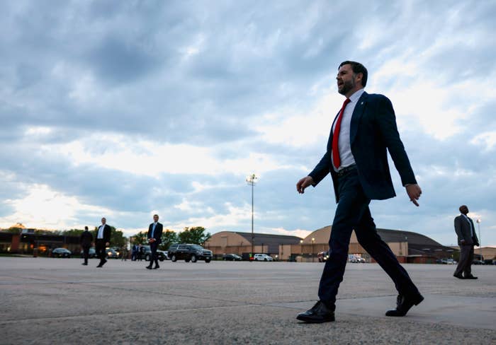 A idiosyncratic   successful  a suit   and reddish  necktie  confidently walks crossed  an unfastened  country  with a partially  cloudy entity  successful  the background