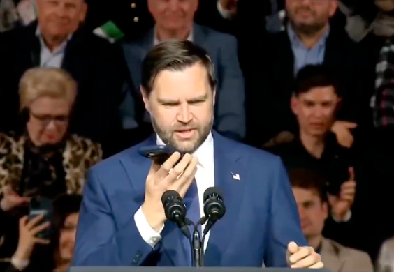 Man successful a suit speaking into a telephone connected talker astatine a podium with microphones, assemblage successful background