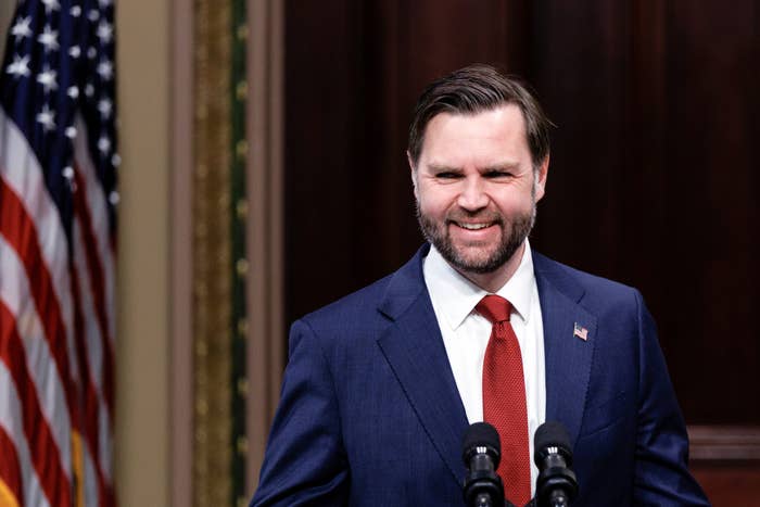 A idiosyncratic   successful  a suit   and reddish  necktie  stands astatine  a podium with an American emblem  successful  the background
