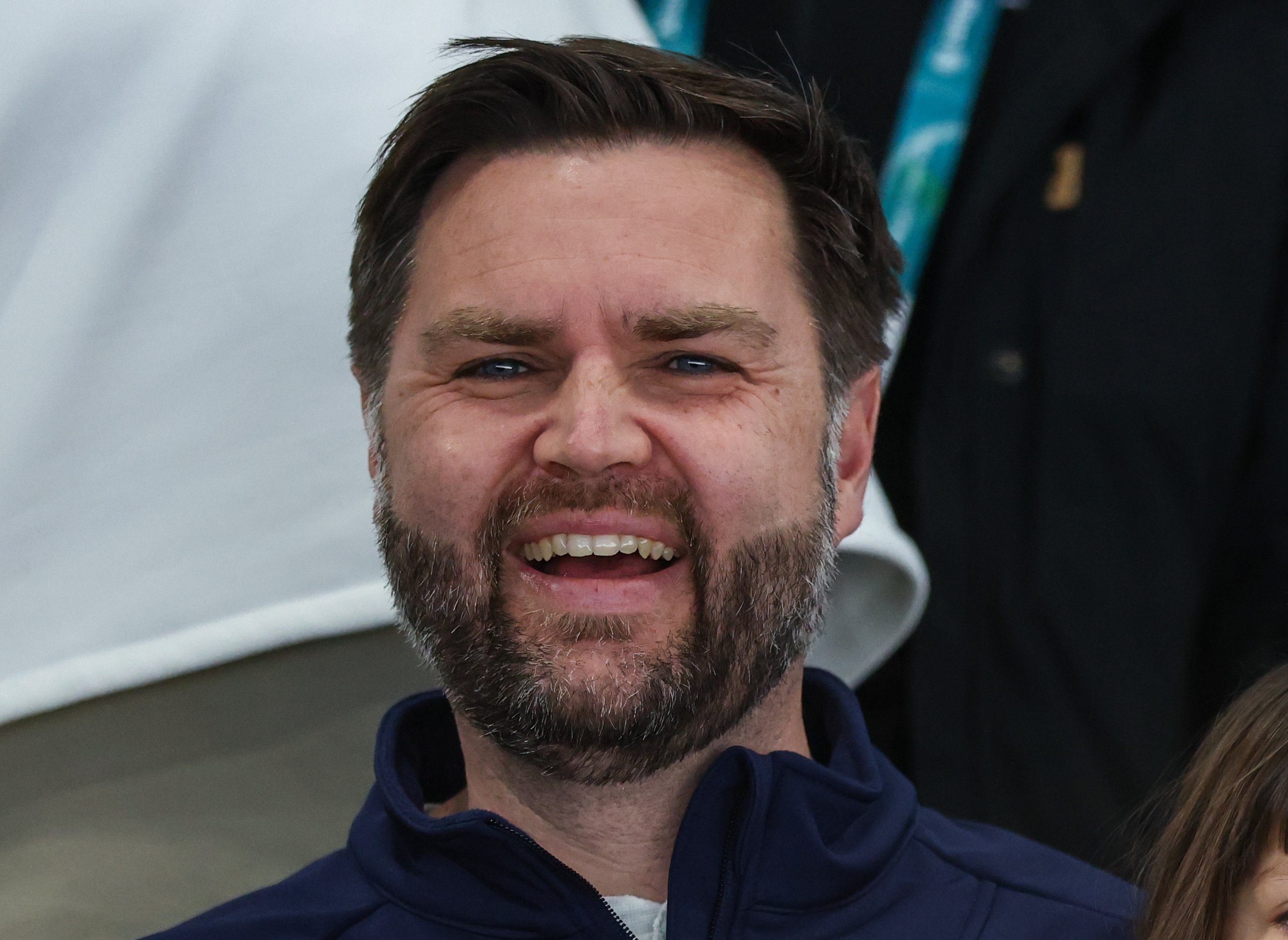 Man smiling, sitting with a young kid connected his lap. He wears a overgarment with a crest and "Vance" embroidered connected it