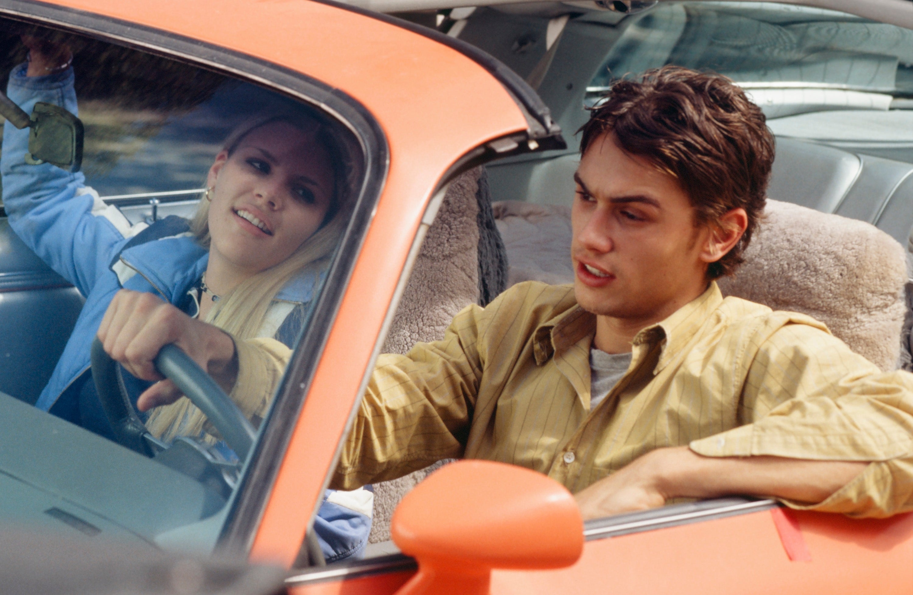  a woman in a casual outfit smiles while the man next to her is driving, looking focused