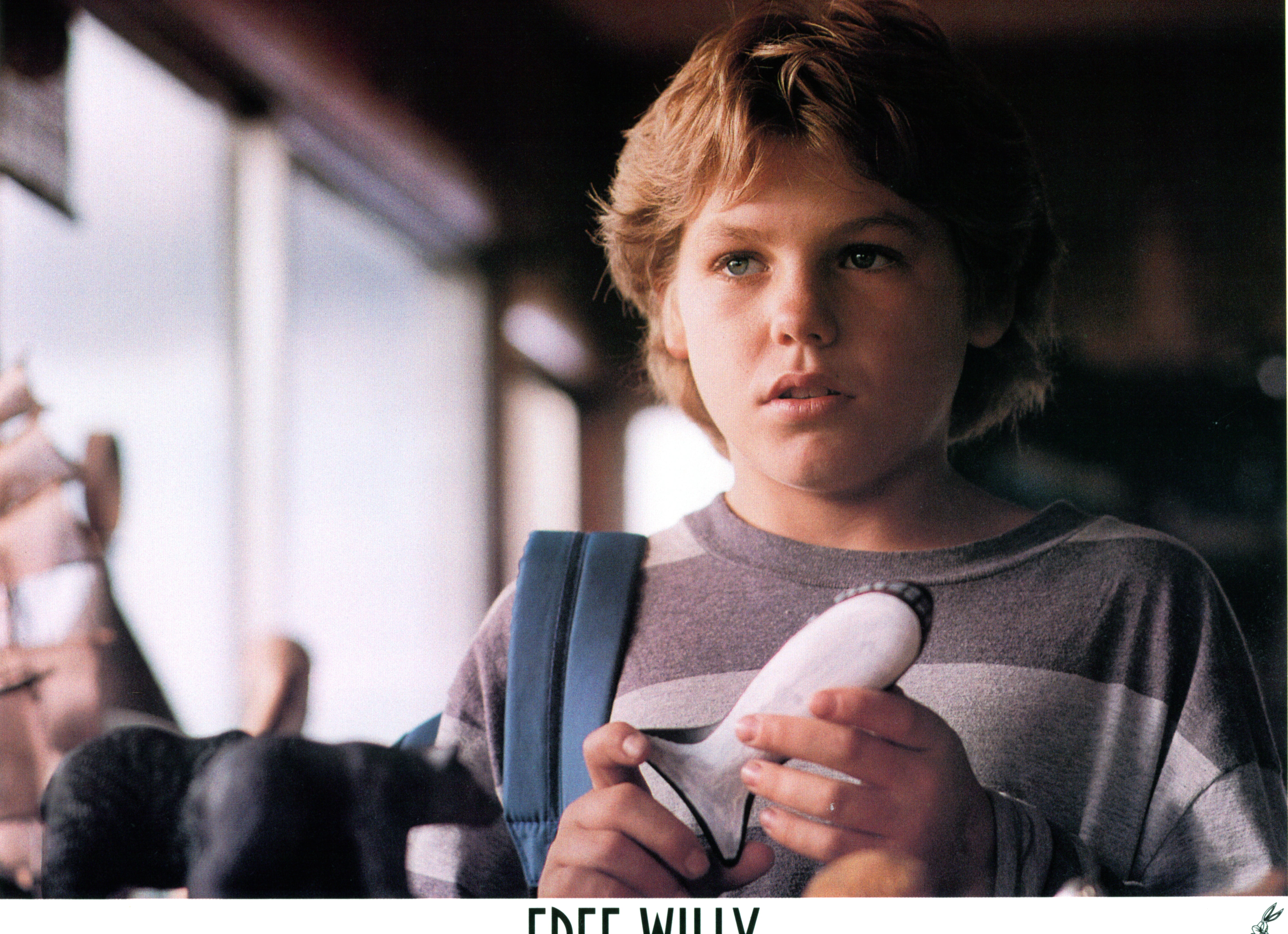A young boy in casual attire holds a small toy whale, looking thoughtful. The setting suggests an indoor environment with soft lighting