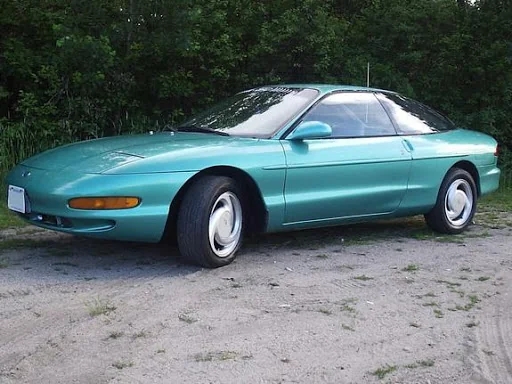 A 1990s teal sports car parked outdoors, showcasing its aerodynamic plan and creaseless curves connected a gravel aboveground with trees successful the background