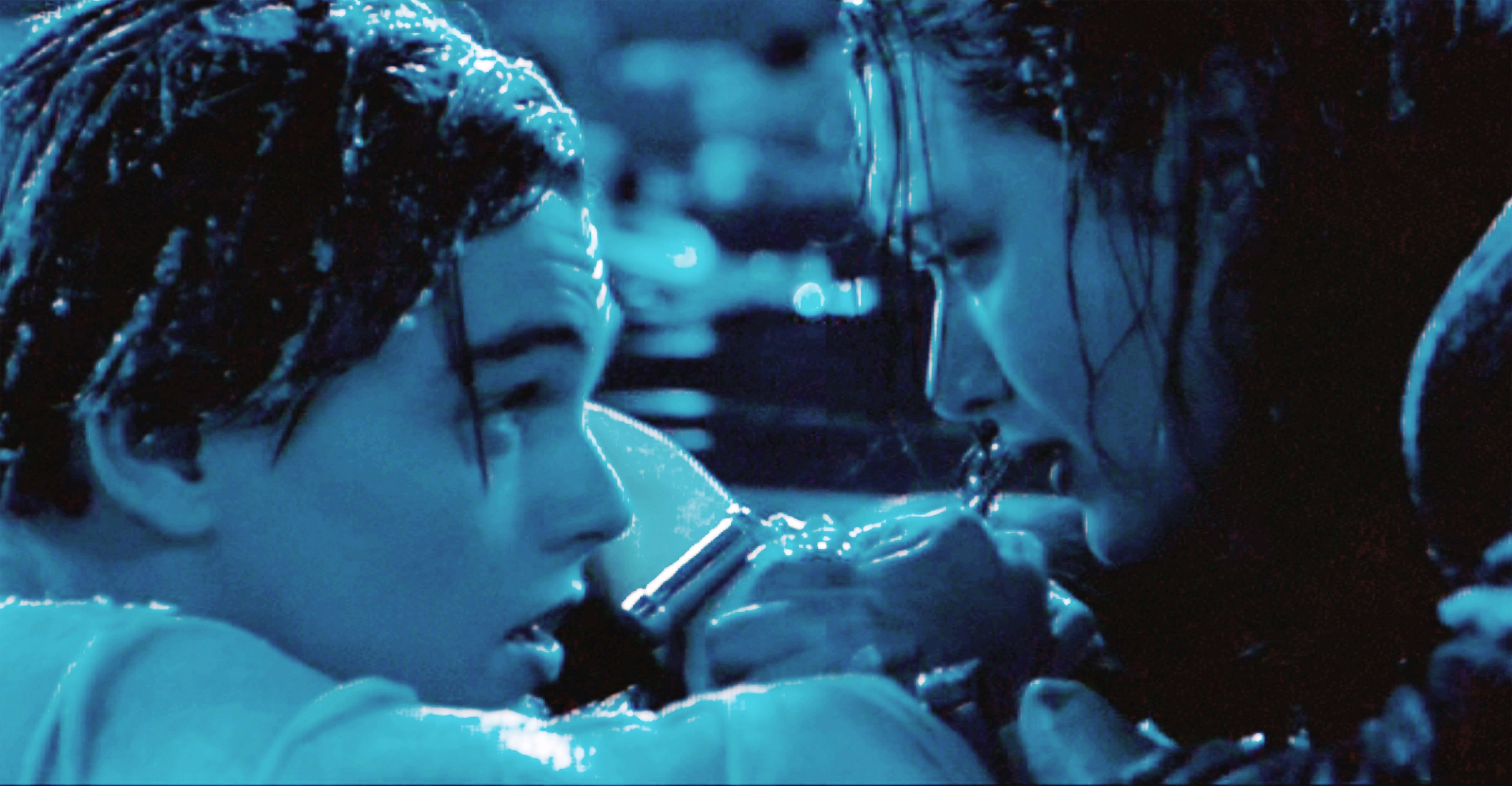 Two people in water hold onto a wooden board, expressing distress and determination. The scene conveys drama and survival