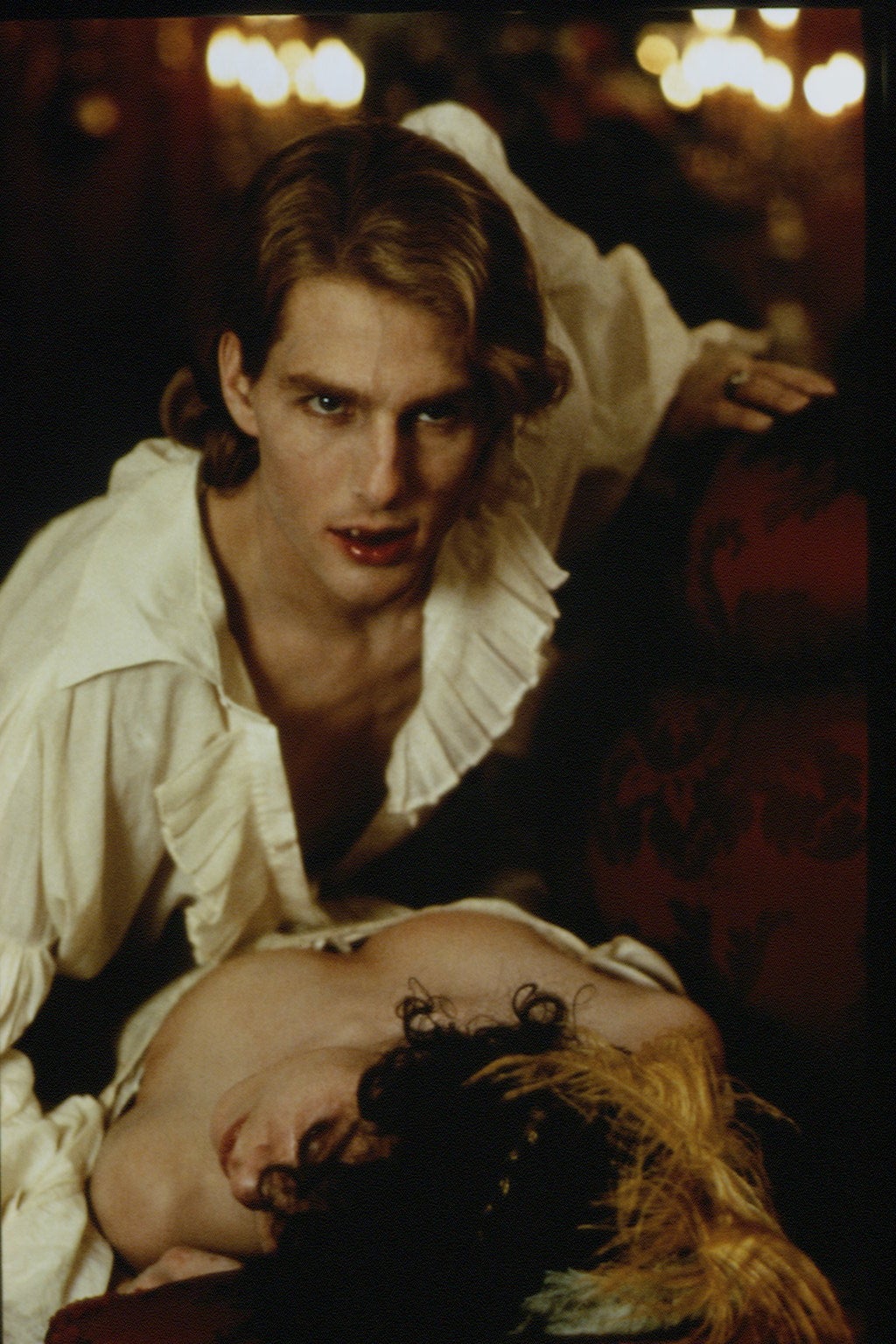 A vampire in an 18th-century-style ruffled shirt leans over a victim on a couch, suggesting a dramatic scene
