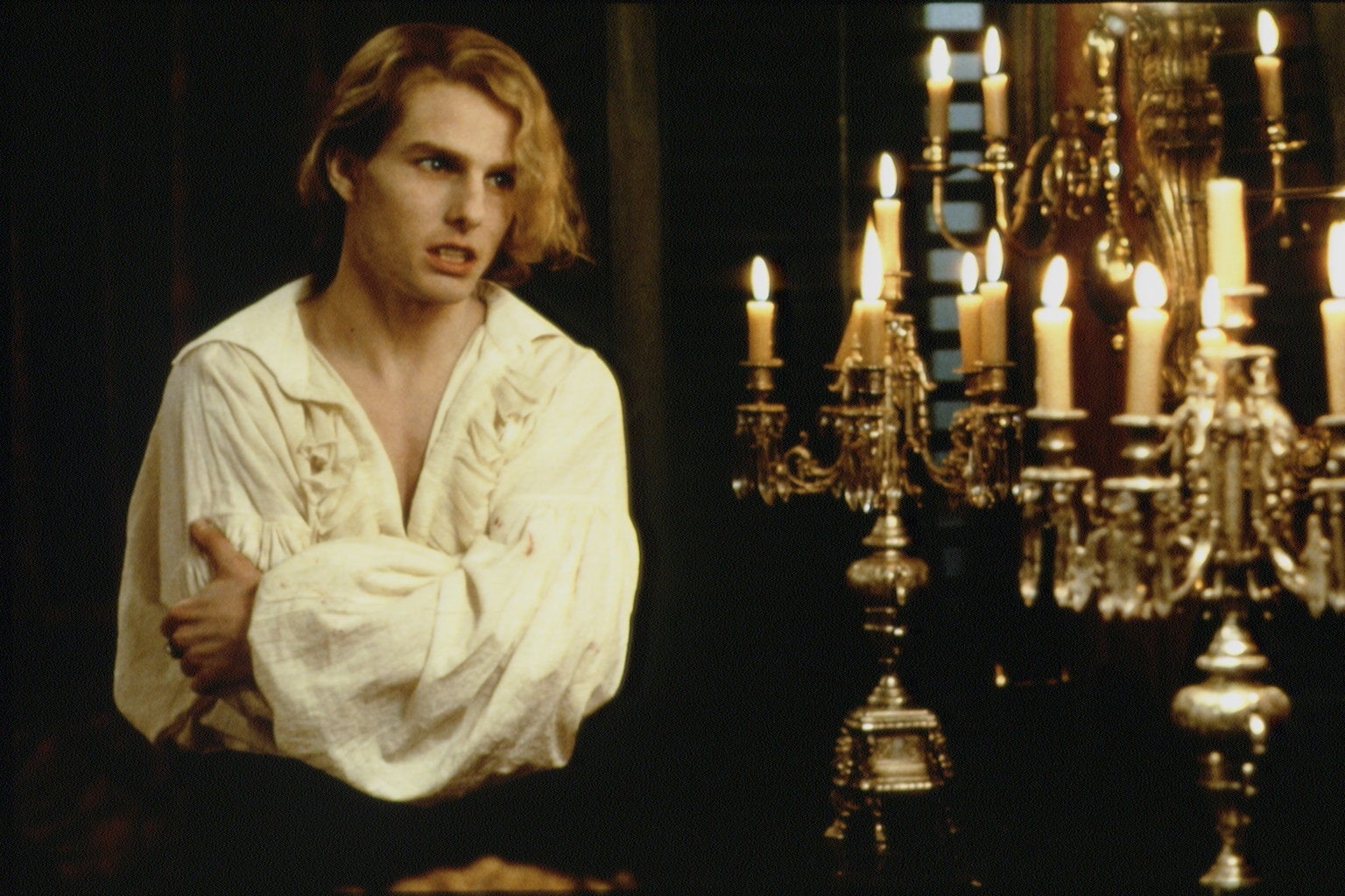 Person in historical clothing stands by ornate candelabra, looking concerned, in a scene suggesting a period drama or film