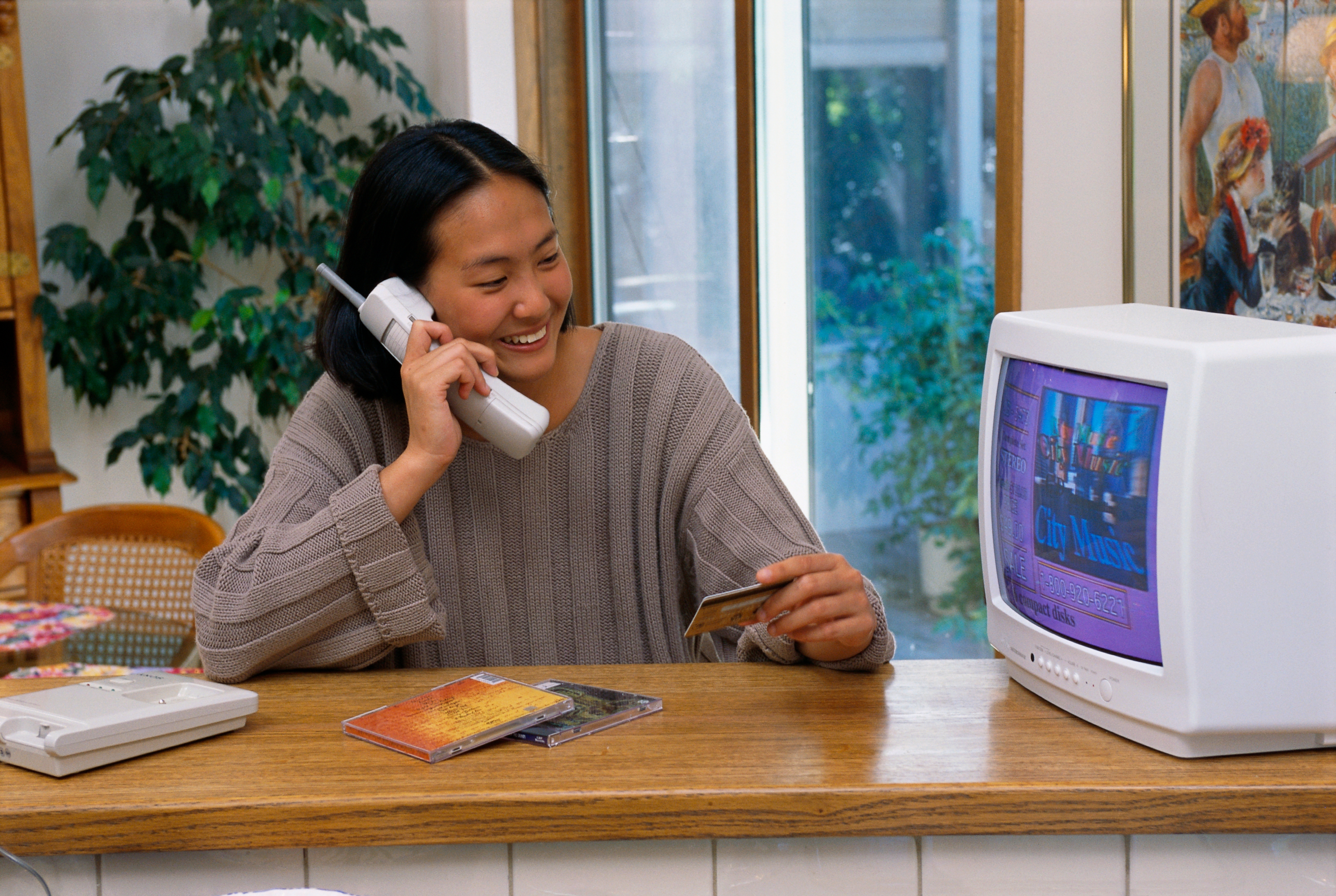 Person successful a sweater smiling portion utilizing a ample cordless telephone and holding a CD lawsuit adjacent a vintage machine and monitor. 90s nostalgia scene