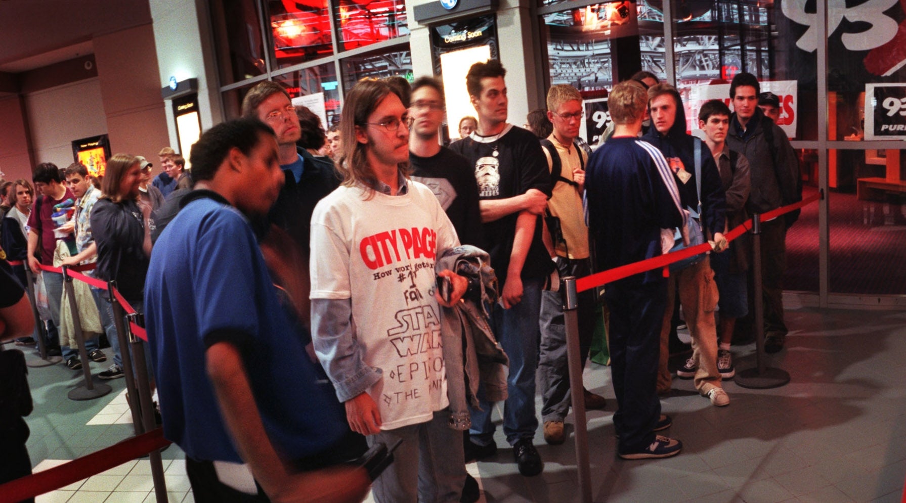 People lined up astatine a theatre summons counter, immoderate wearing themed T-shirts. Staff assists customers, with posters and lights successful the background
