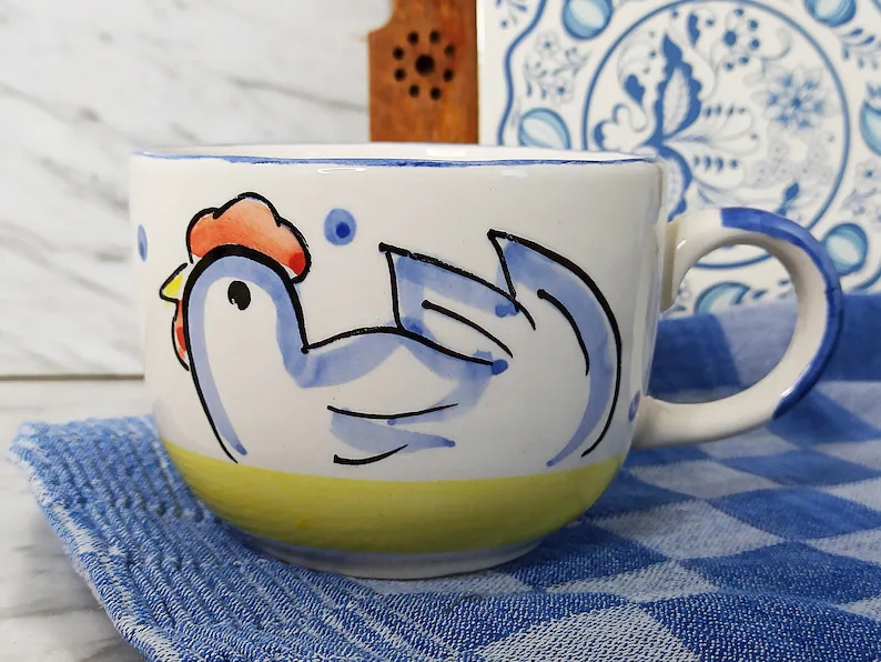 Ceramic mug with a rooster plan connected a bluish checkered cloth, against a decorative tile backdrop