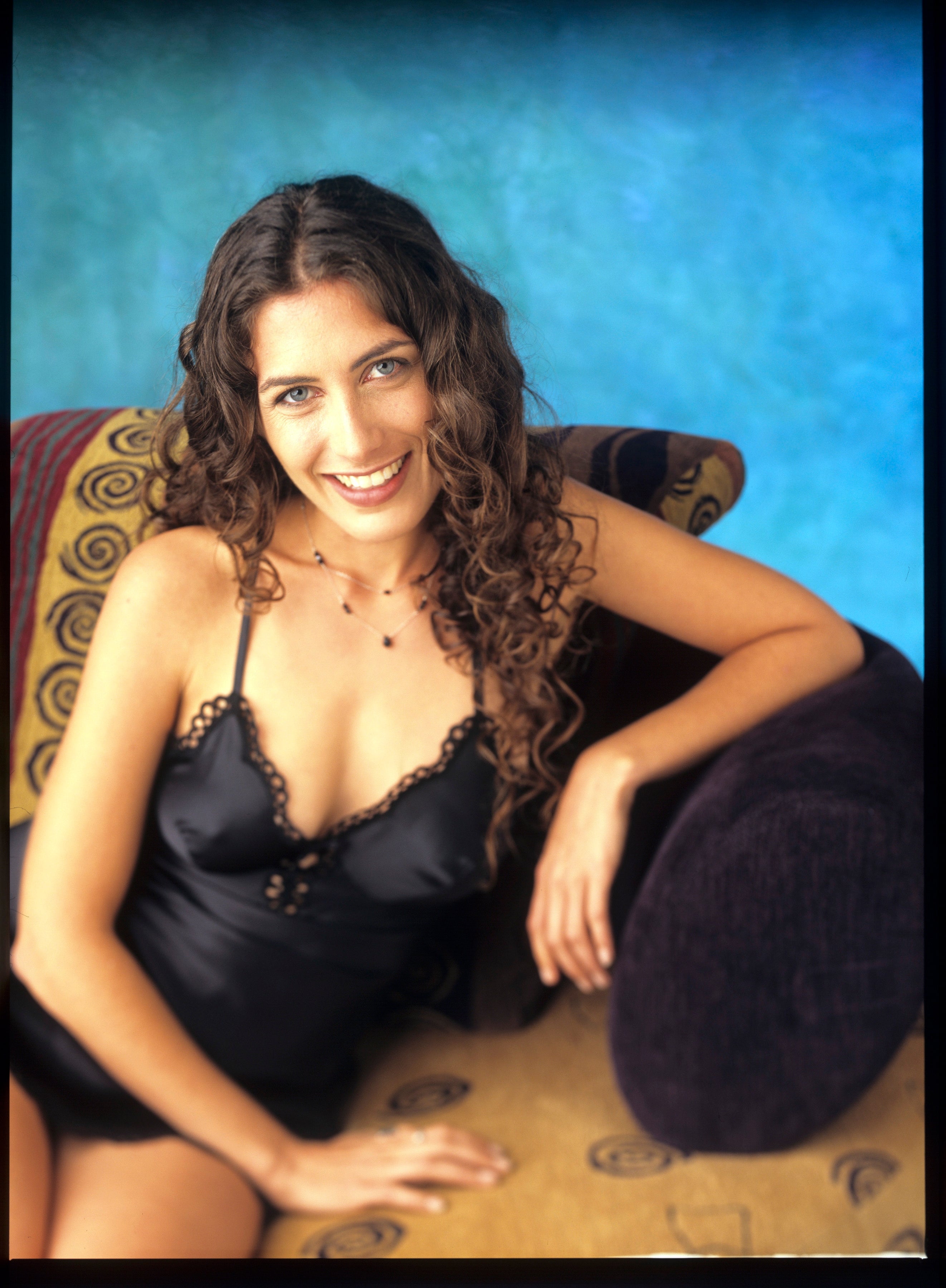 Person sitting and smiling on a patterned couch, wearing a stylish, lace-trimmed outfit