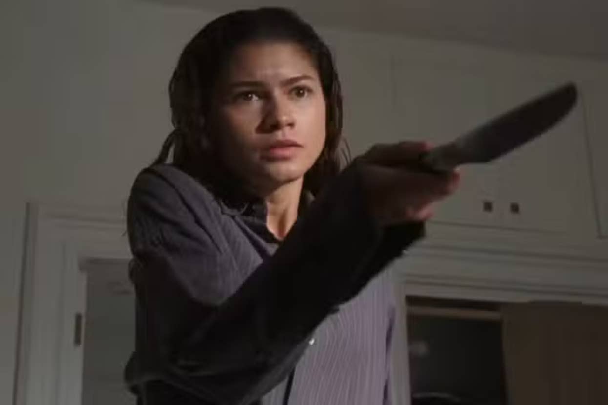 Person in a striped shirt pointing a knife indoors, appearing focused and intense