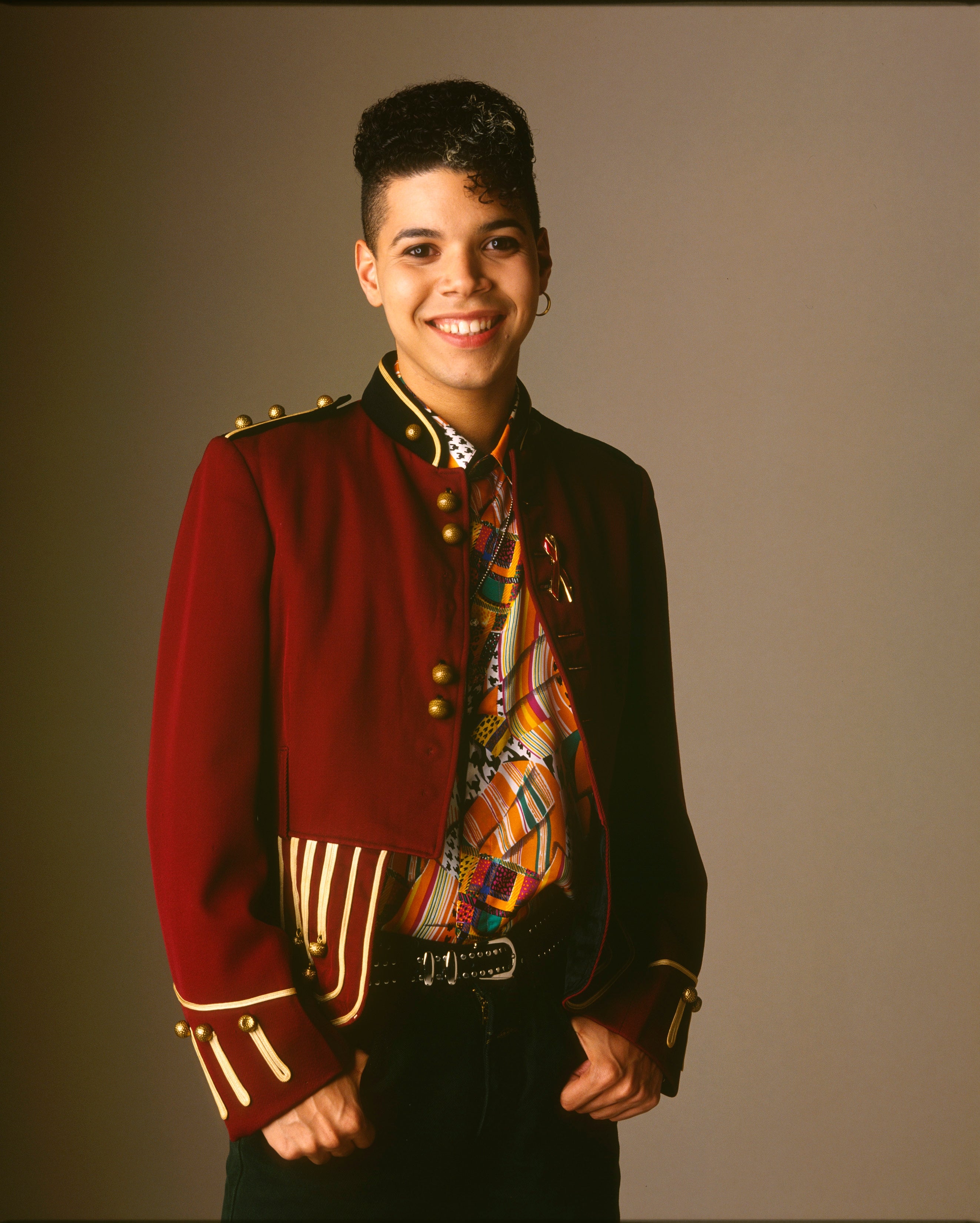 Person wearing a stylish military-inspired jacket over a patterned shirt, smiling confidently