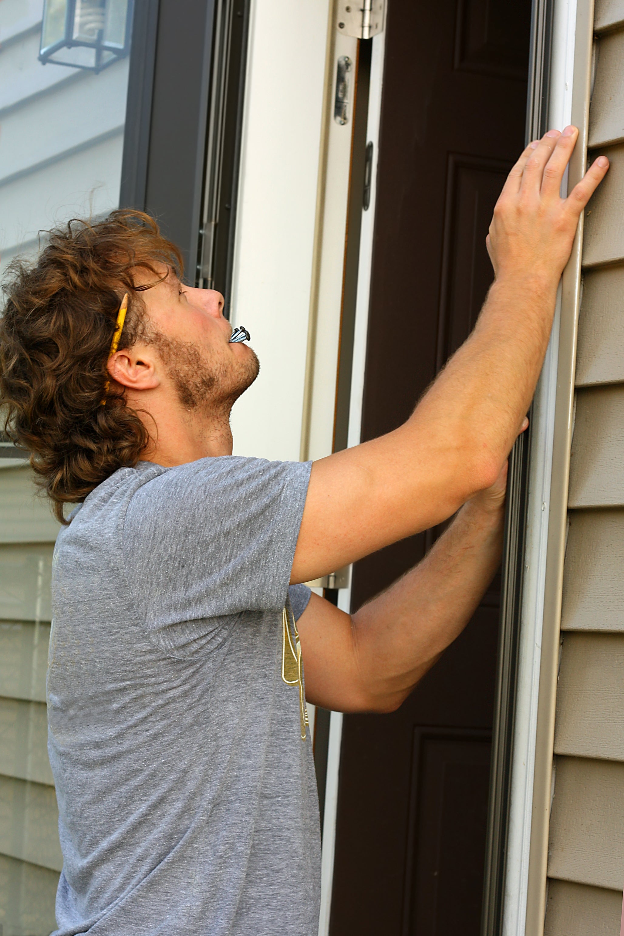 Person in a casual T-shirt works on installing or inspecting a door frame, holding a pencil behind their ear