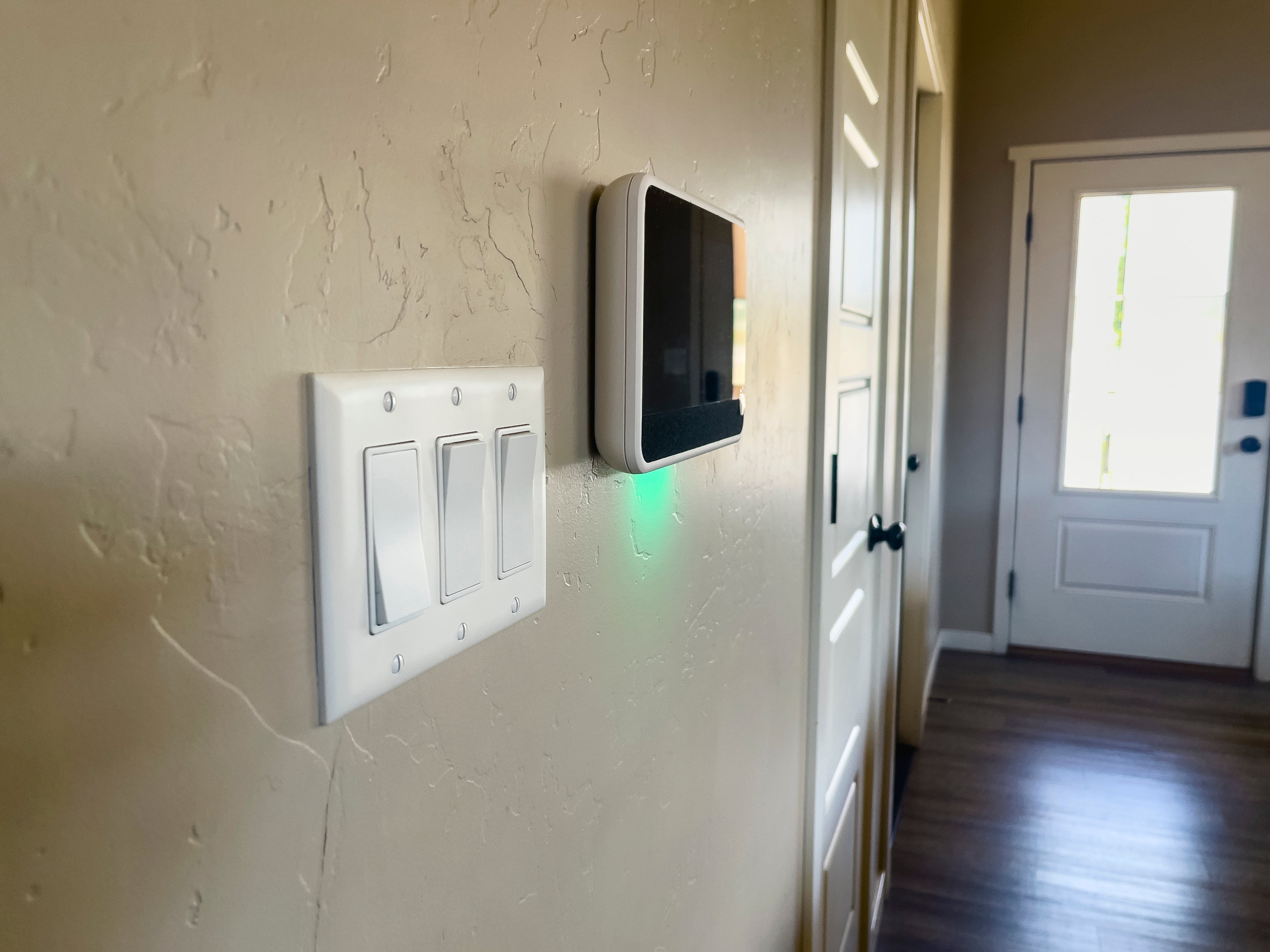 Light switches and a smart thermostat mounted on a wall in a home hallway
