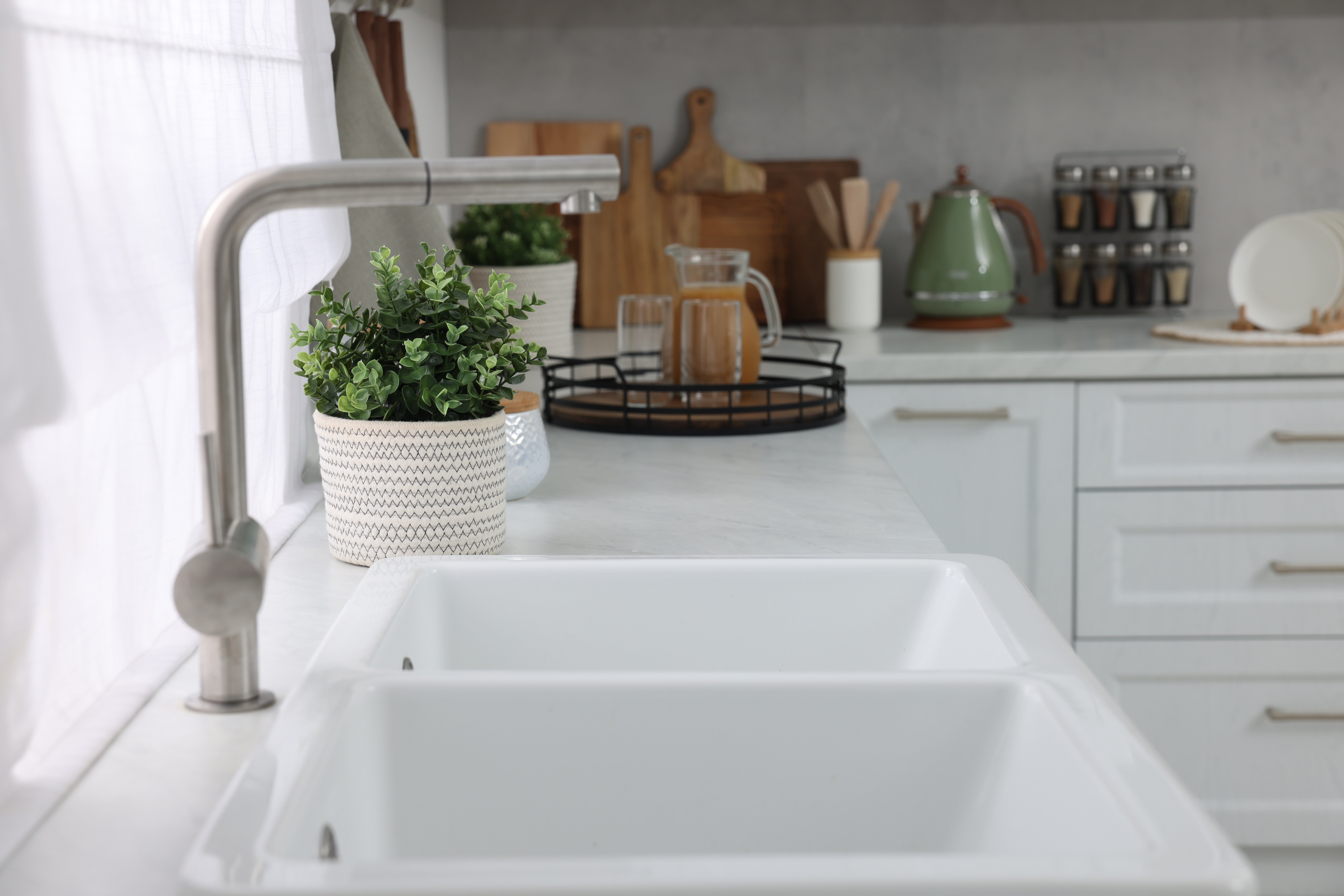 Modern kitchen with white sink, potted plant, and wooden cooking utensils