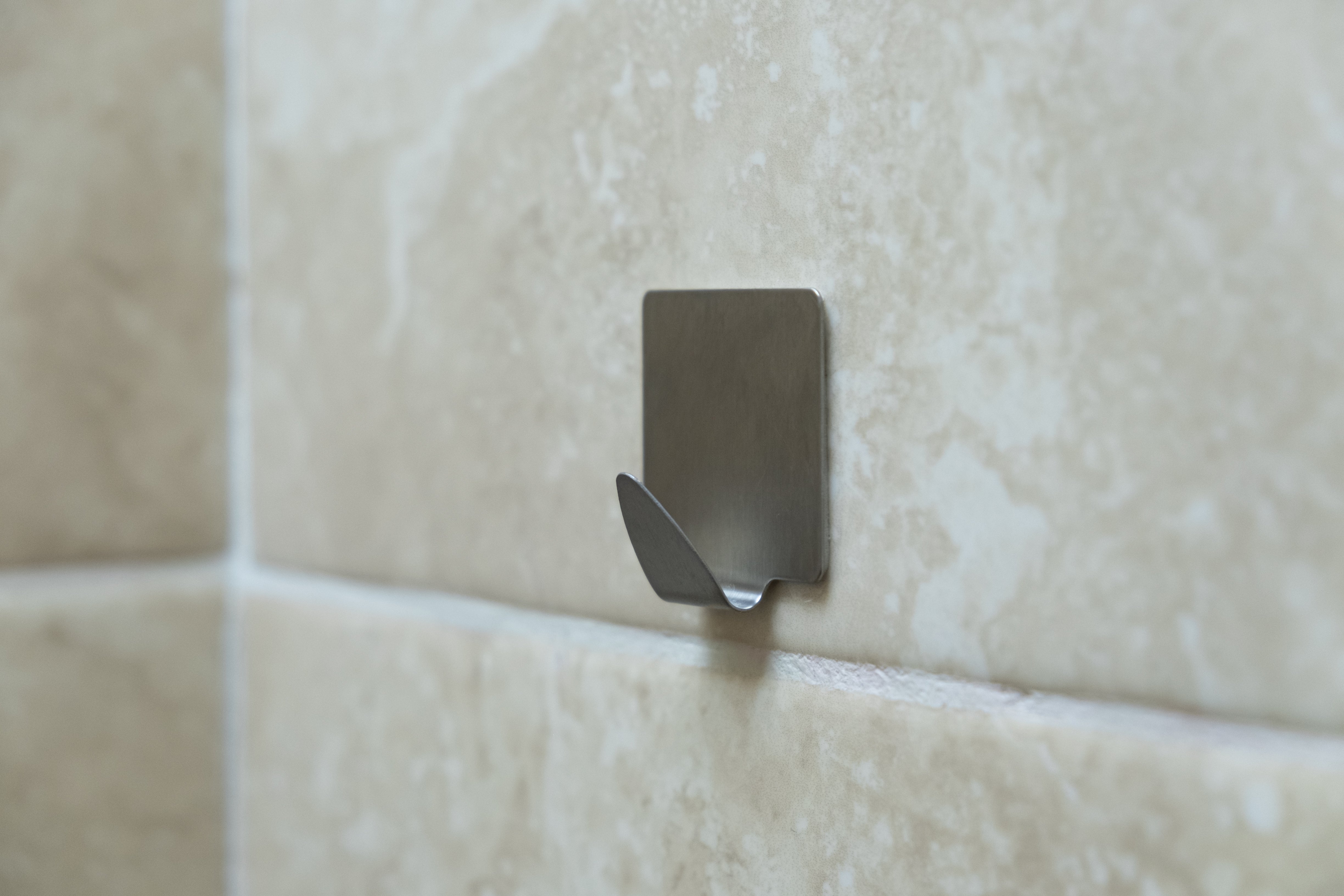 Metal wall hook attached to tiled wall, shown in a close-up view
