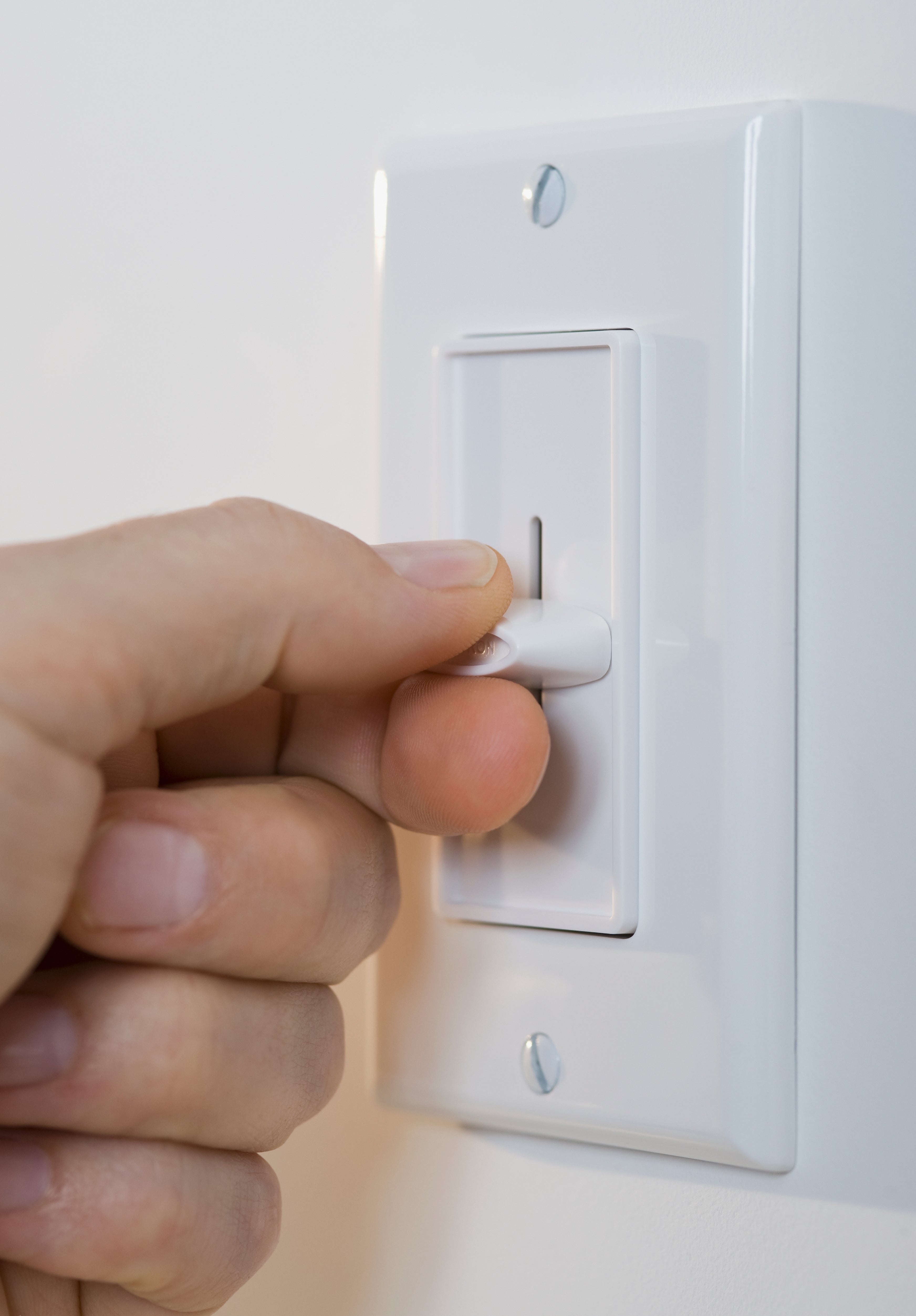 Close-up of a hand adjusting a white dimmer light switch on a wall