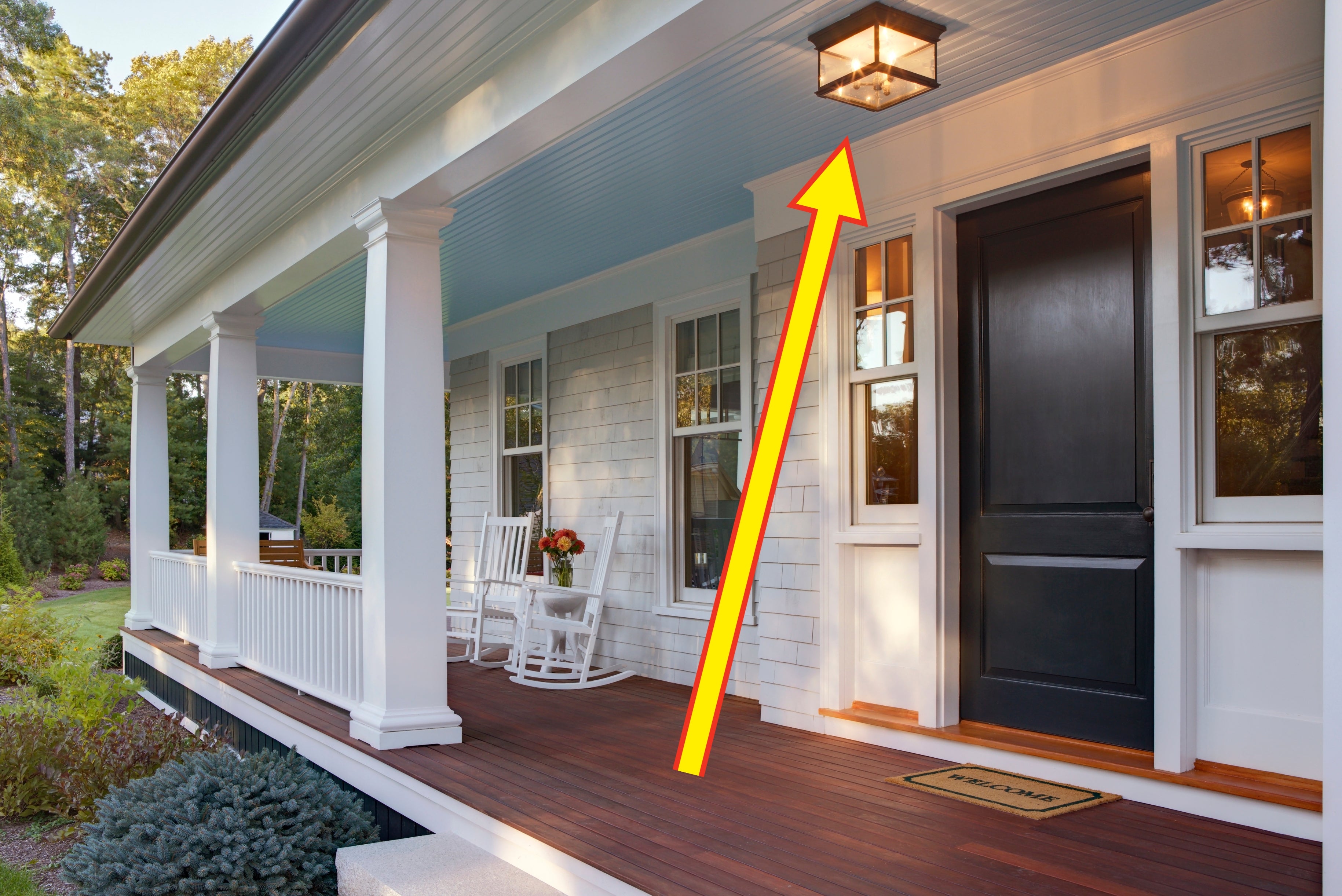 Front porch with a white rocking chair, potted plant, and "Welcome" mat near a dark door. Appears calm and inviting