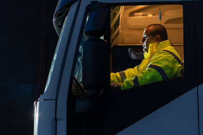 Truck operator  successful  a reflective overgarment   sits focused successful  the cab, captured successful  illustration   presumption    astatine  night
