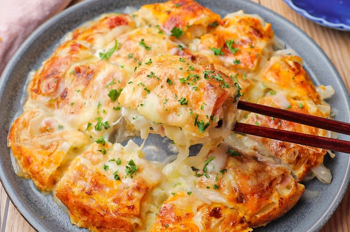 テーブルに盛り付けられたチーズがとろける玉ねぎ料理を箸で持ち上げるシーン。