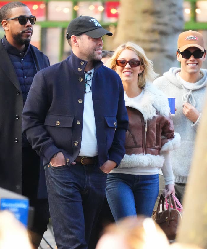 Group of radical   walking outdoors, including a idiosyncratic   successful  a fur-trimmed overgarment   and sunglasses, and different  successful  a chapeau  and sunglasses, looking relaxed