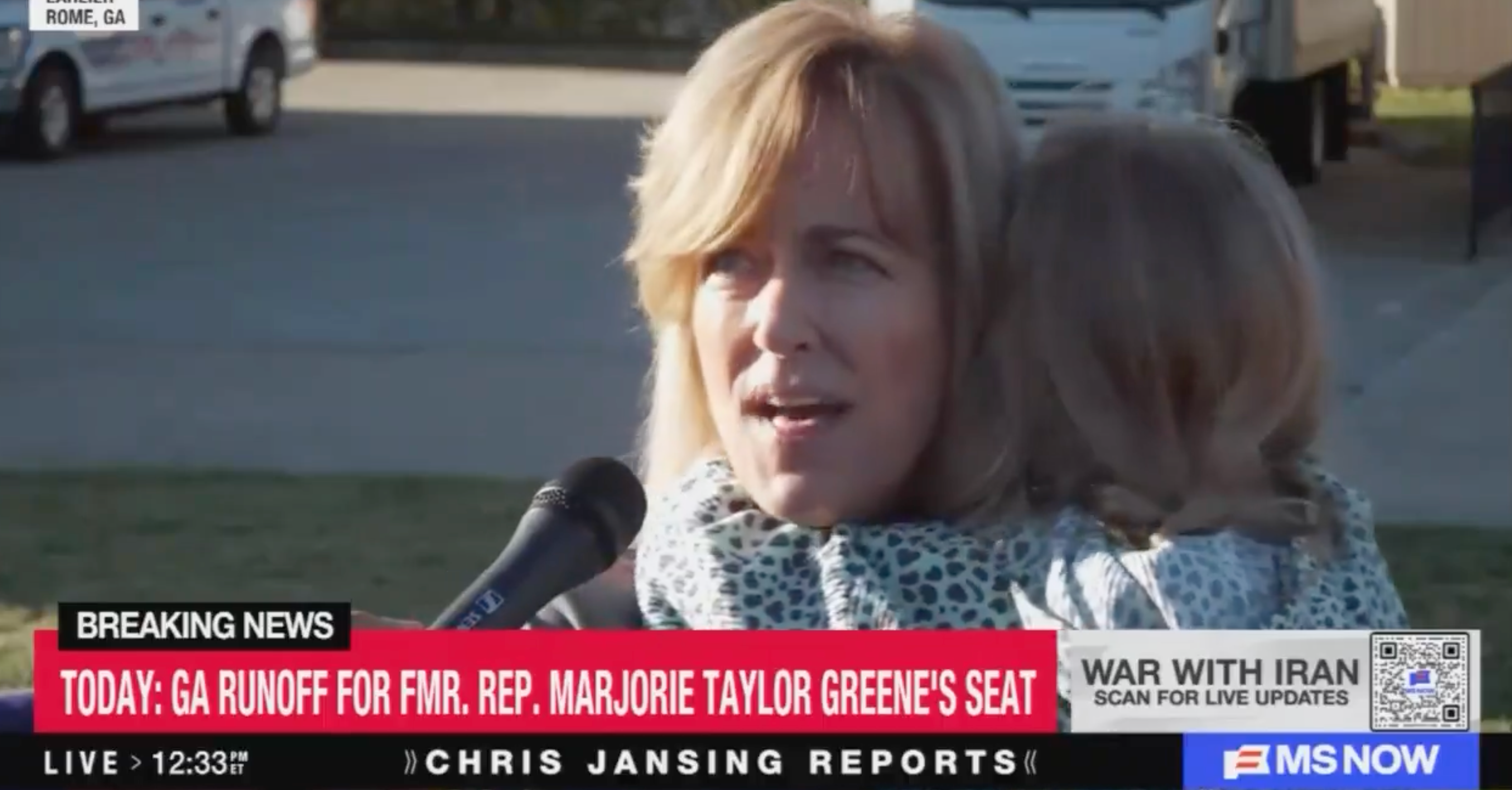 En person som snakker i en mikrofon, holder et barn. Nyhetsticker nevner GA-avrenning for et kongresssete