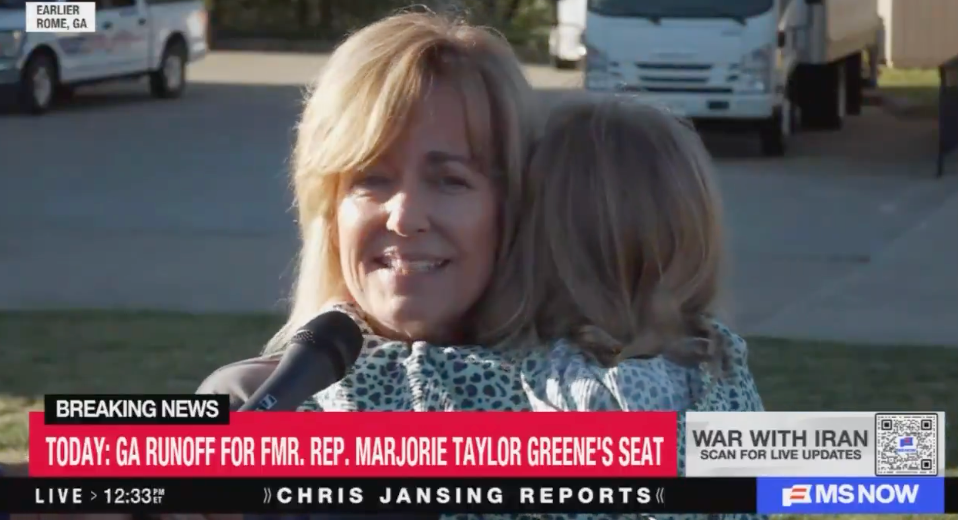 En kvinne som holder et barn snakker ved en mikrofon under en nyhetshendelse. Nyhetsbanneret nevner Georgia-avrenningen for Marjorie Taylor Greenes sete