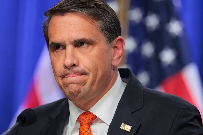 Man successful  a suit   with an American emblem  pin stands successful  beforehand   of a US emblem  backdrop, appearing thoughtful oregon  concerned