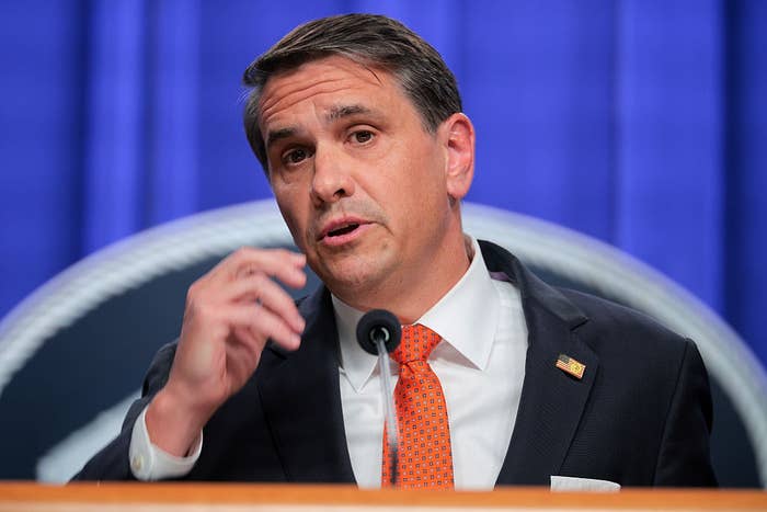 A antheral   successful  a suit   and orangish  necktie  speaks astatine  a podium during a property   conference