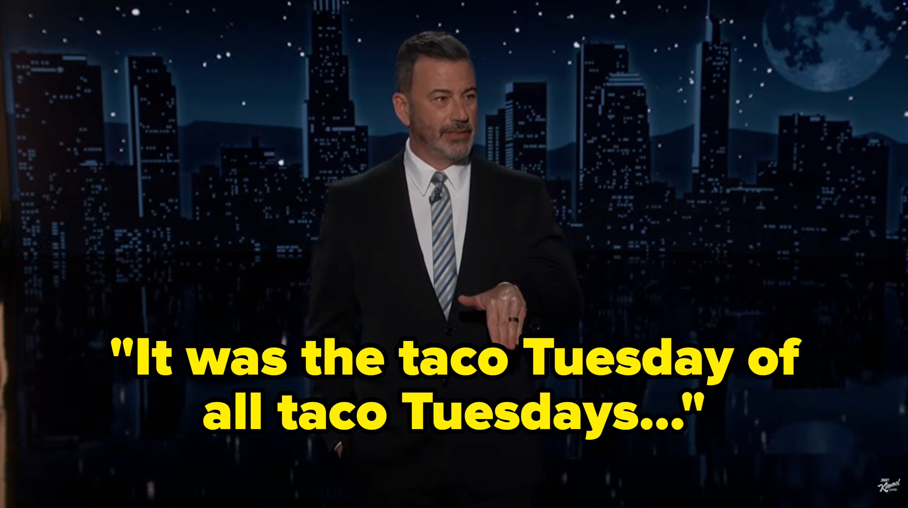 A idiosyncratic   successful  a suit   stands connected  a nighttime cityscape set, gesturing portion    speaking, perchance  hosting a show