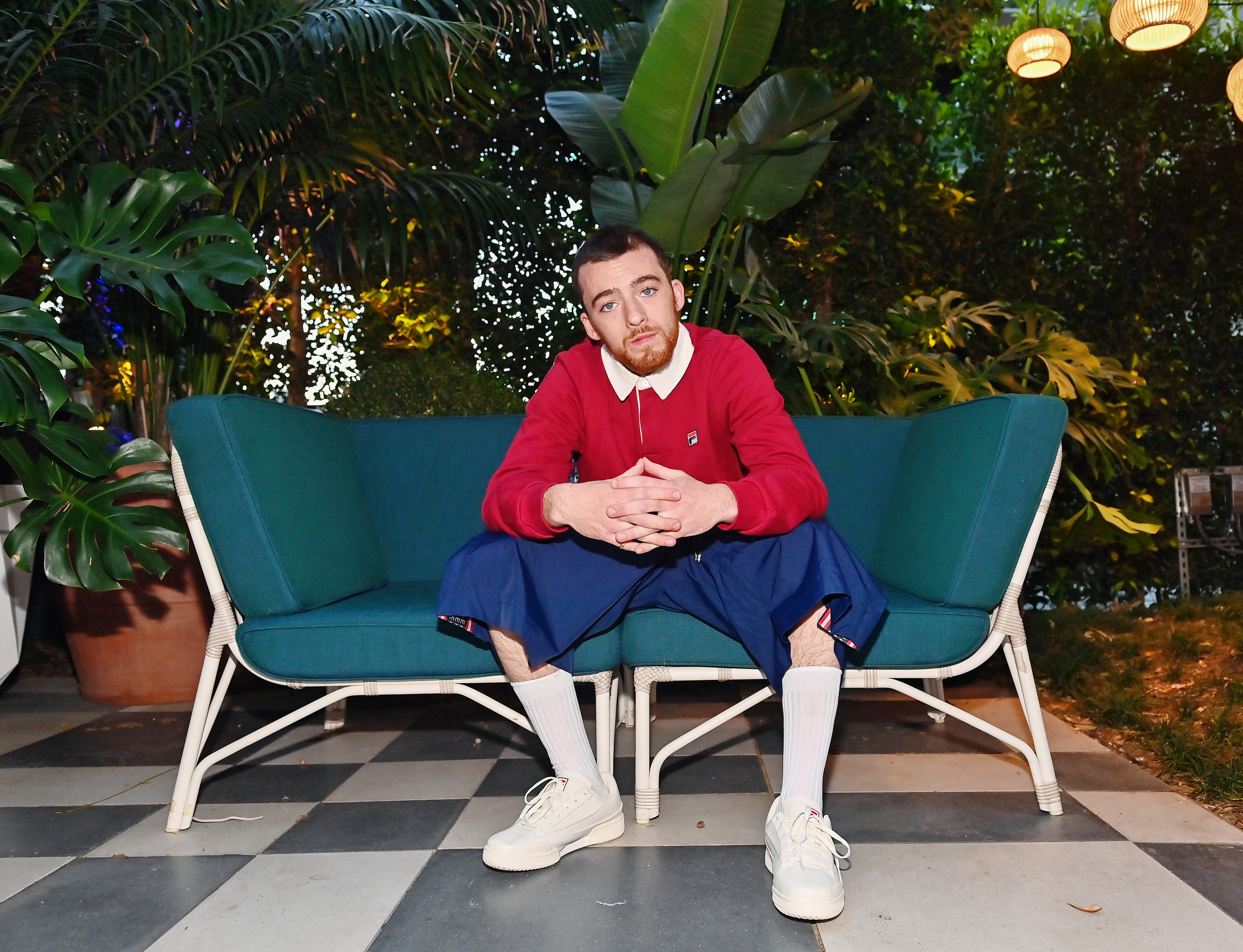 Person successful casual attire sits connected an outdoor sofa with plants successful the background