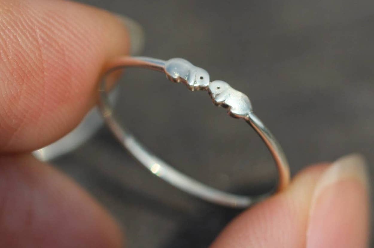 Close-up of a delicate ring featuring two small otters touching noses, crafted in a minimalist style. Suitable for animal lovers or as a gift