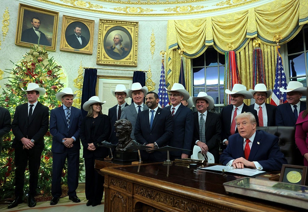 Gruppe mennesker i cowboyhatter i det ovale kontor med presidenten sittende ved skrivebordet sitt, juletre i bakgrunnen
