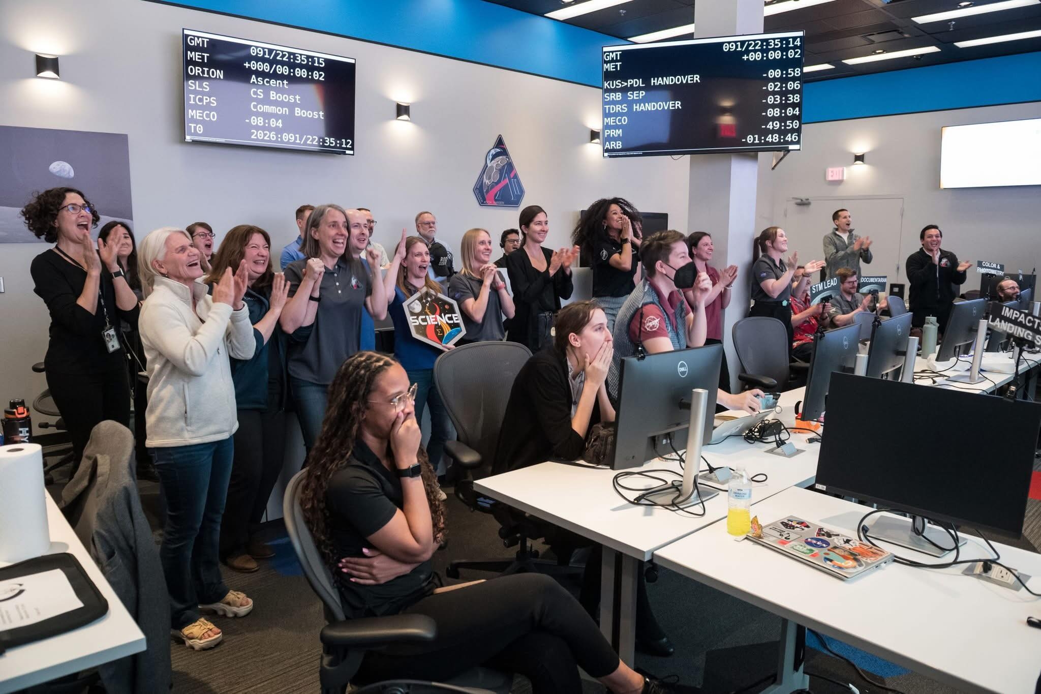 People successful a power country cheer and applaud, watching a palmy ngo lawsuit connected screens above. Various individuals show excitement and relief
