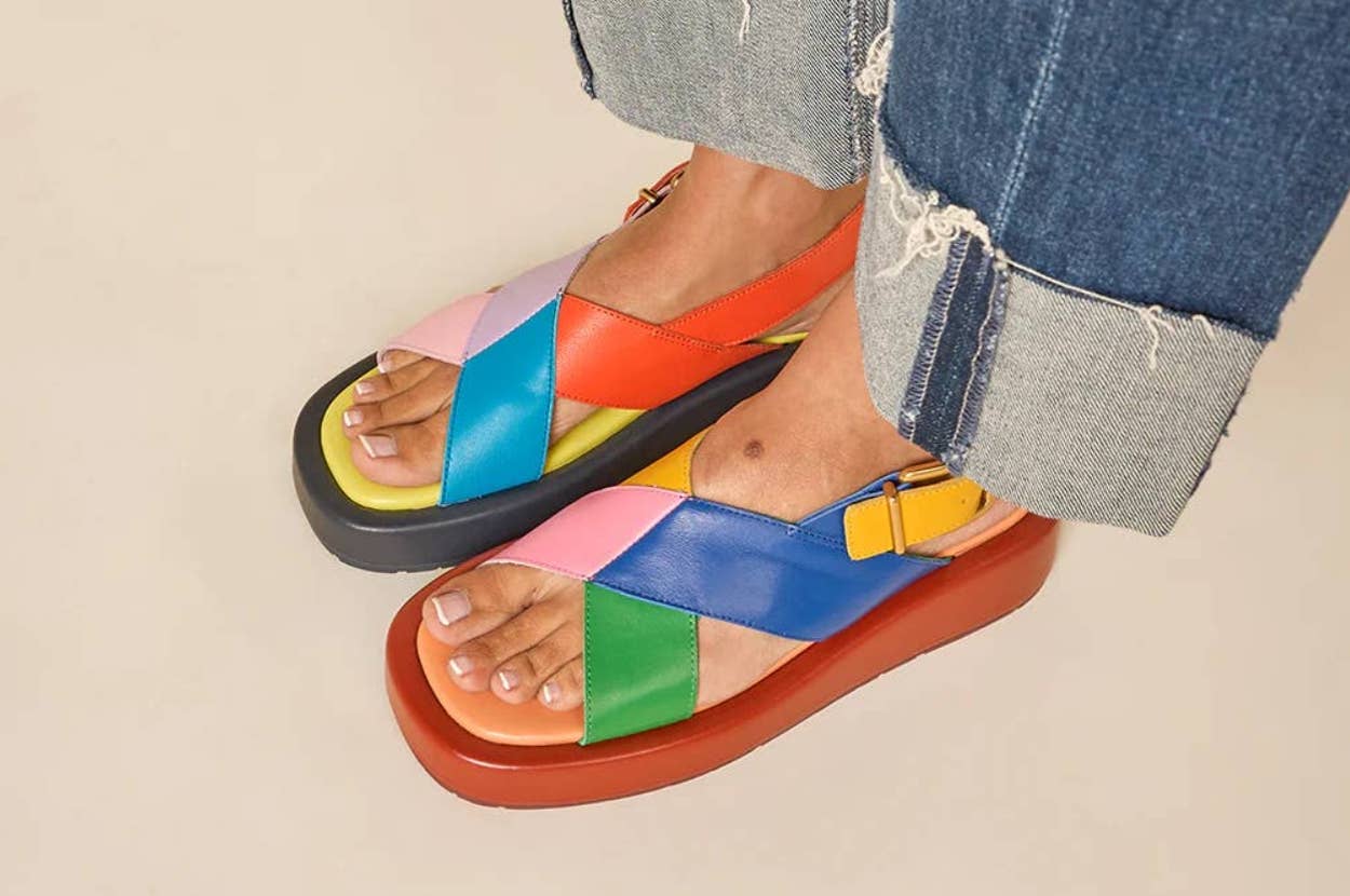 Person wearing vibrantly colored, crisscross strap sandals with a thick sole; styled with cuffed denim jeans. Ideal for a bold, casual look