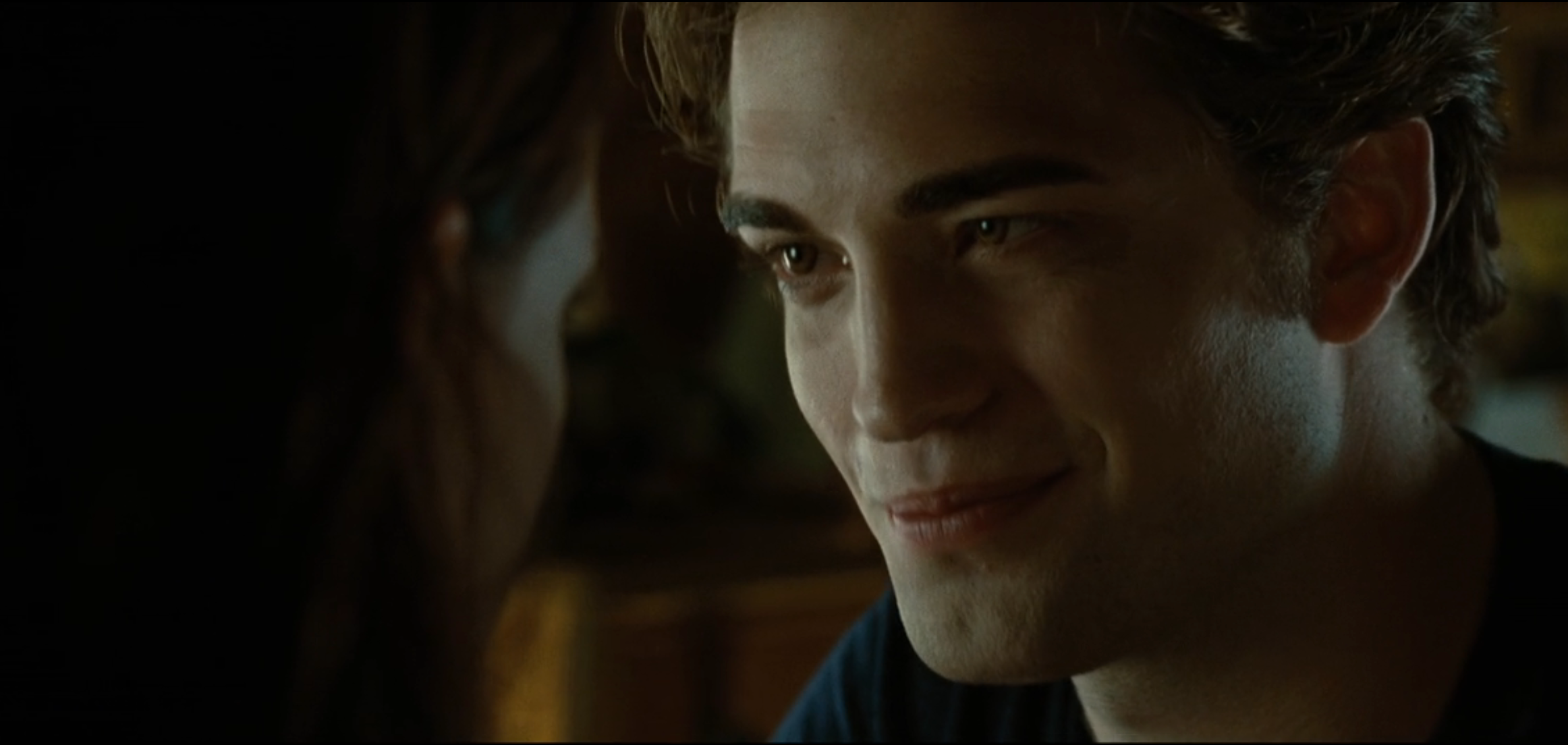 En person med et mildt smil ser på en annen person i et svakt opplyst miljø. Intim og fokusert atmosfære